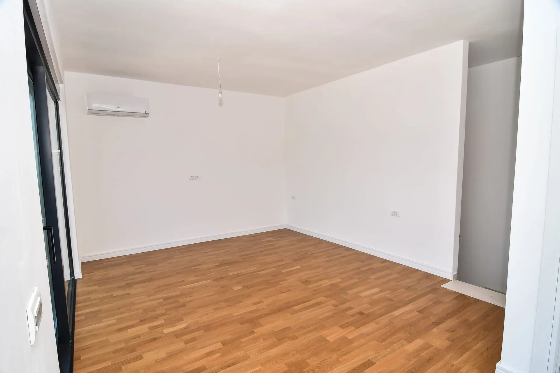 Salon lumineux avec parquet et climatisation dans une nouvelle villa à Budva, Monténégro. Pièce vide avec finition blanche.