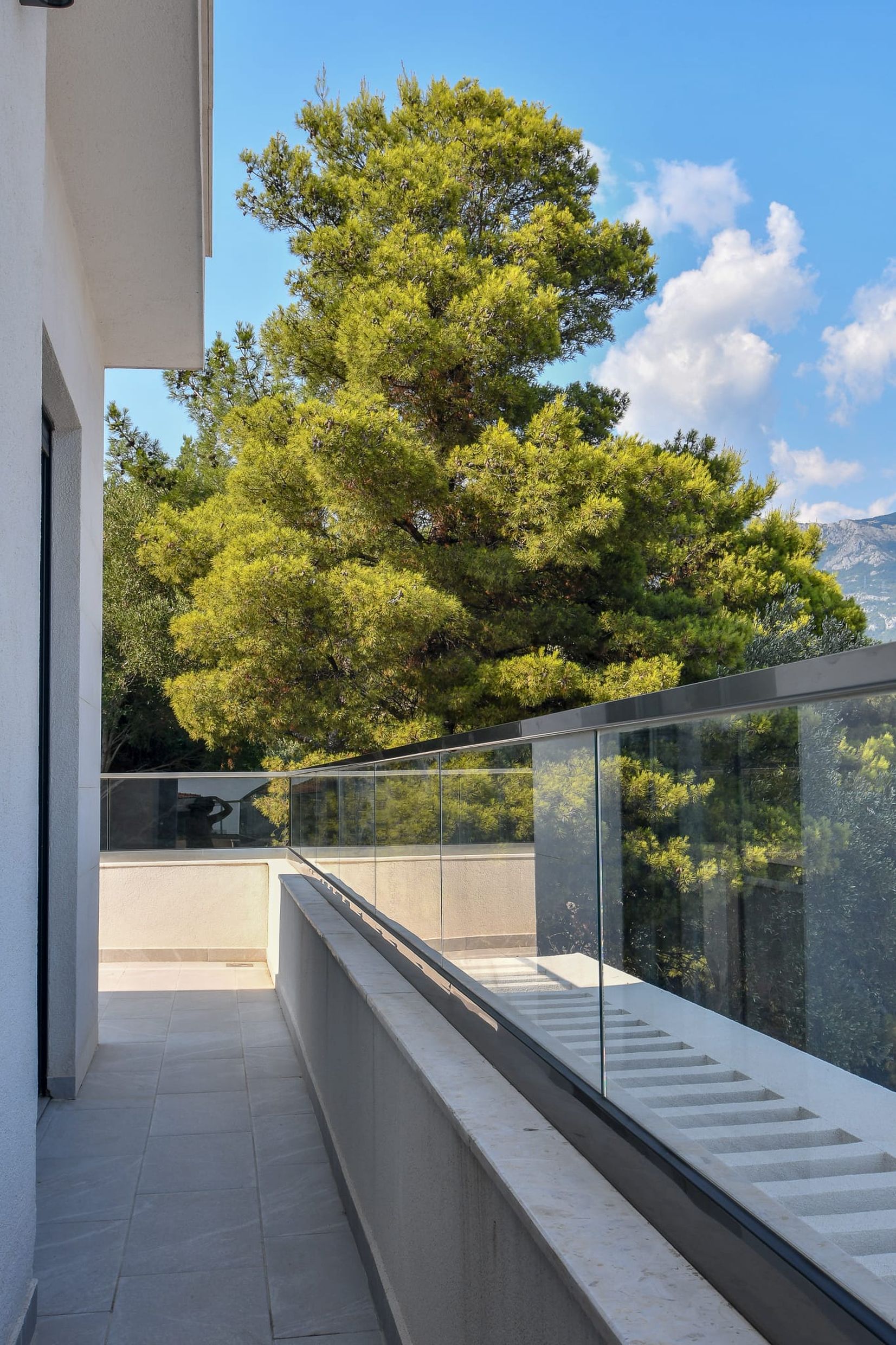 Geräumiger Balkon mit Panoramaverglasung und Blick auf Nadelbäume in einer Villa in Budva, Montenegro.