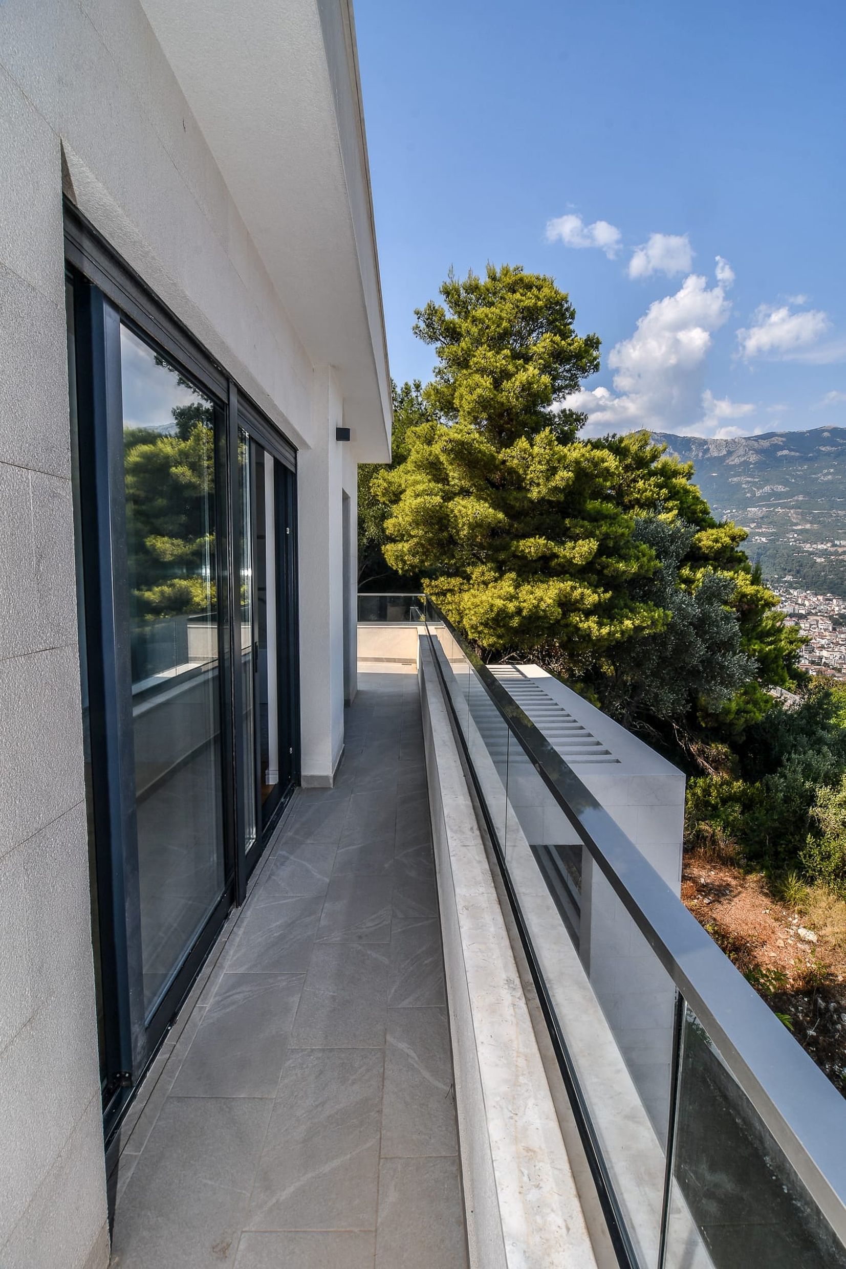 Moderner Balkon einer Villa in Budva, Montenegro, mit Panoramaverglasung, Steinboden und Blick auf die Berge und das Meer.