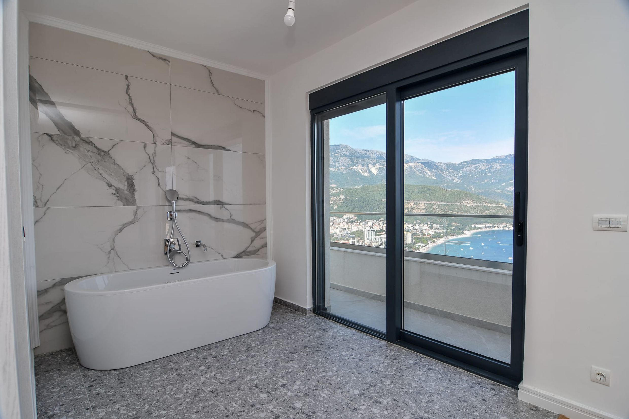 Badezimmer mit Panoramablick auf das Meer und die Berge in einer Villa, Budva, Montenegro: freistehende Badewanne und Marmoroptik-Fliesen.