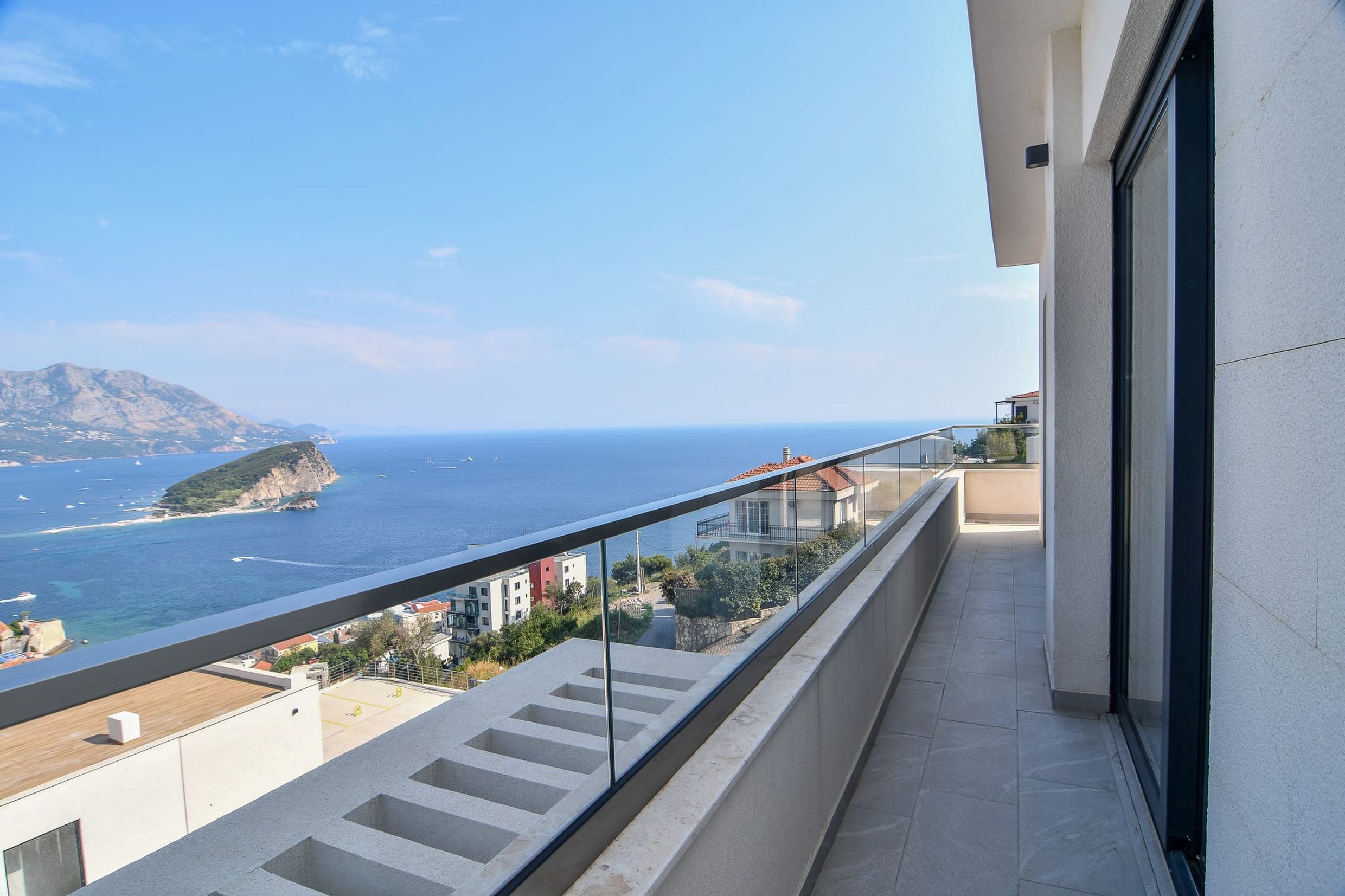 Geräumiger Balkon mit Panoramablick auf das Meer und die Insel in Budva, Montenegro: moderne Ausstattung und Glasgeländer.