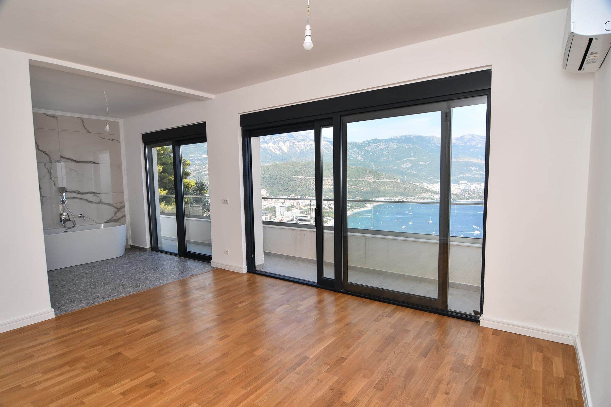 Wohnzimmer mit Panoramablick auf das Meer und die Berge in einer Villa in Budva, Montenegro, mit Badewanne am Fenster und Parkettboden.