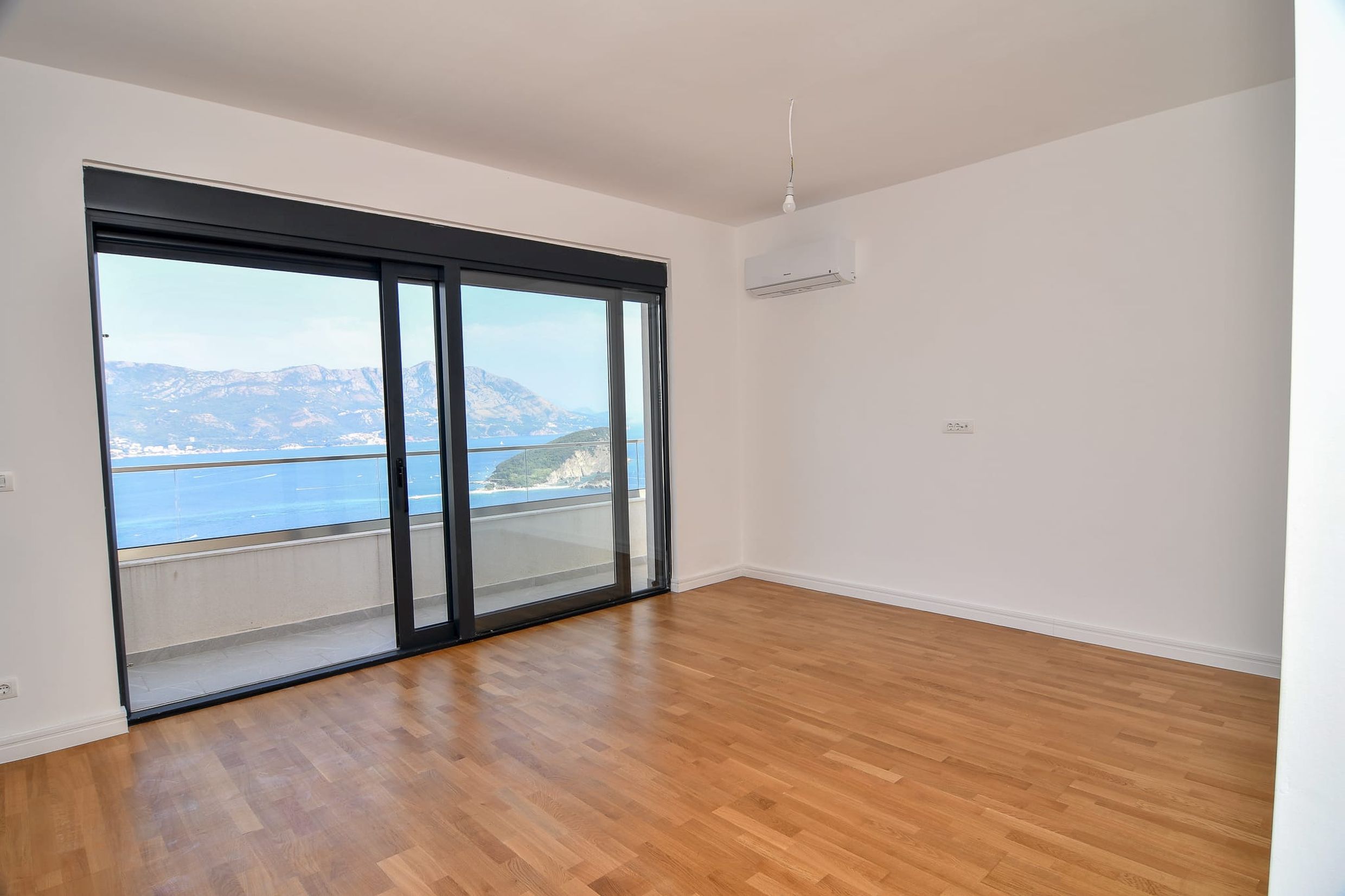 Helles Wohnzimmer mit Panoramablick auf das Meer und die Berge in der Villa Budva, Montenegro: Parkett, Balkon und Klimaanlage.