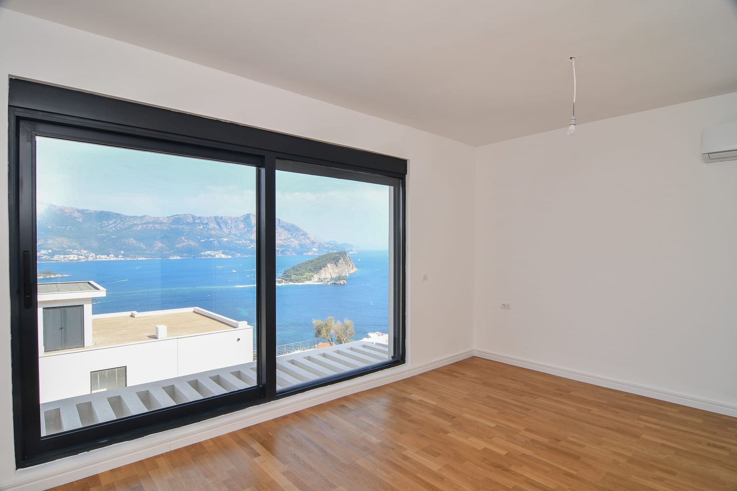 Helles Wohnzimmer mit Panoramablick auf das Meer und die Insel in Budva, Montenegro: Parkettboden, große Fenster, Klimaanlage.