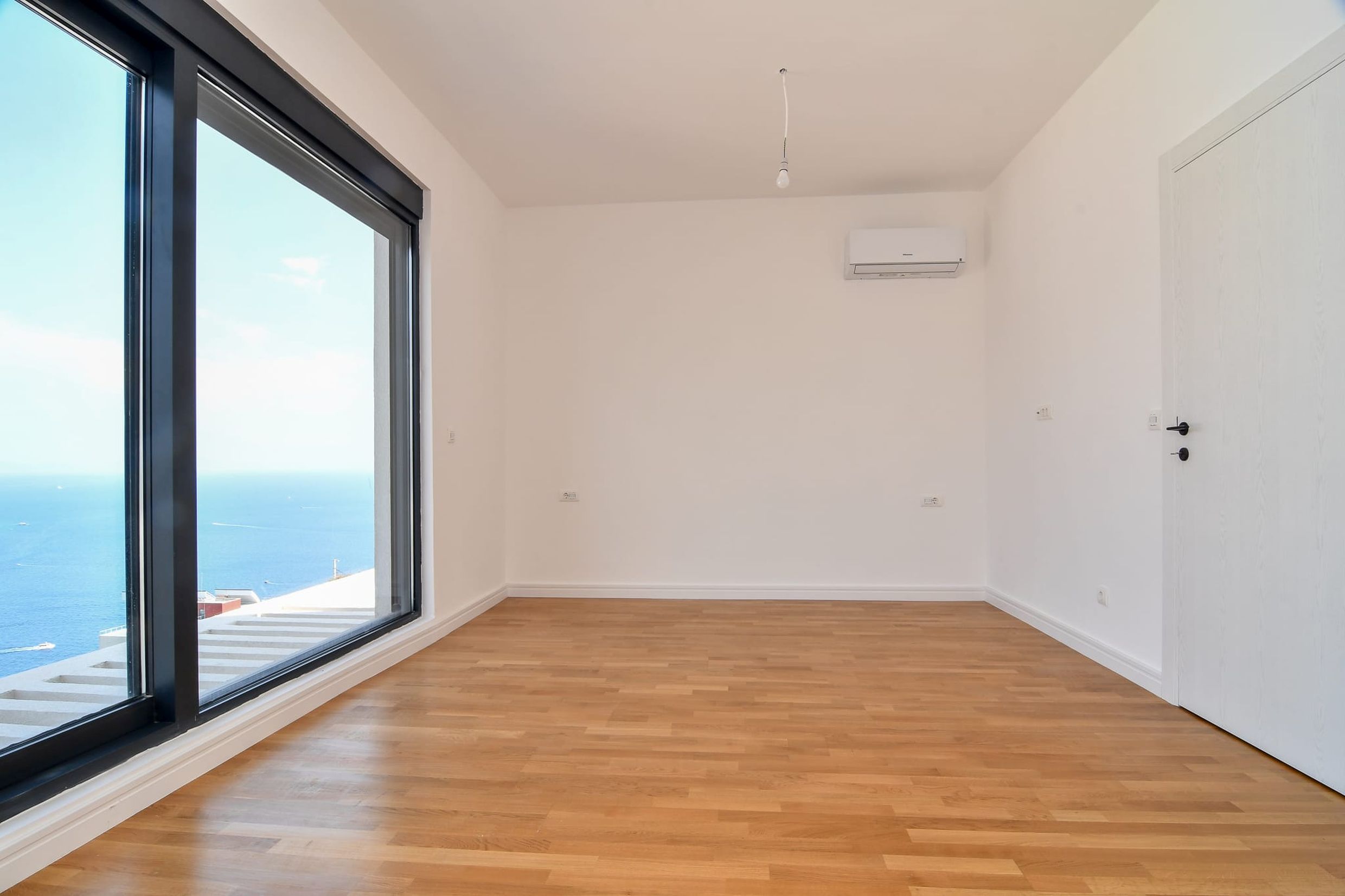 Leeres Schlafzimmer mit Panoramablick auf das Meer in einer Villa, Budva, Montenegro: helle Ausstattung, Parkett und Klimaanlage.