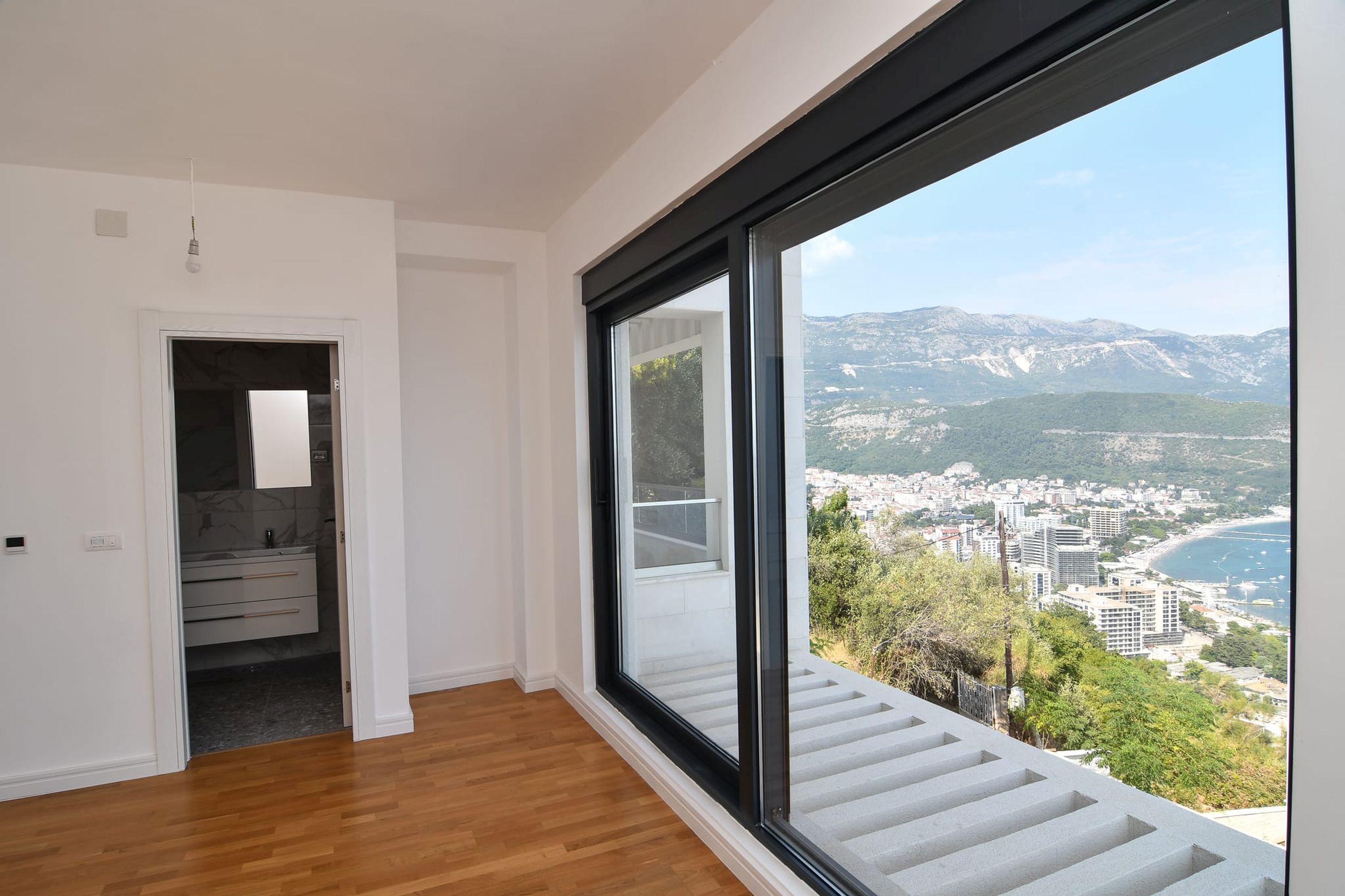 Schlafzimmer mit Panoramafenster und Blick auf das Meer und die Berge in einer Villa, Stadt Budva, Montenegro. Modernes Interieur mit Parkett.