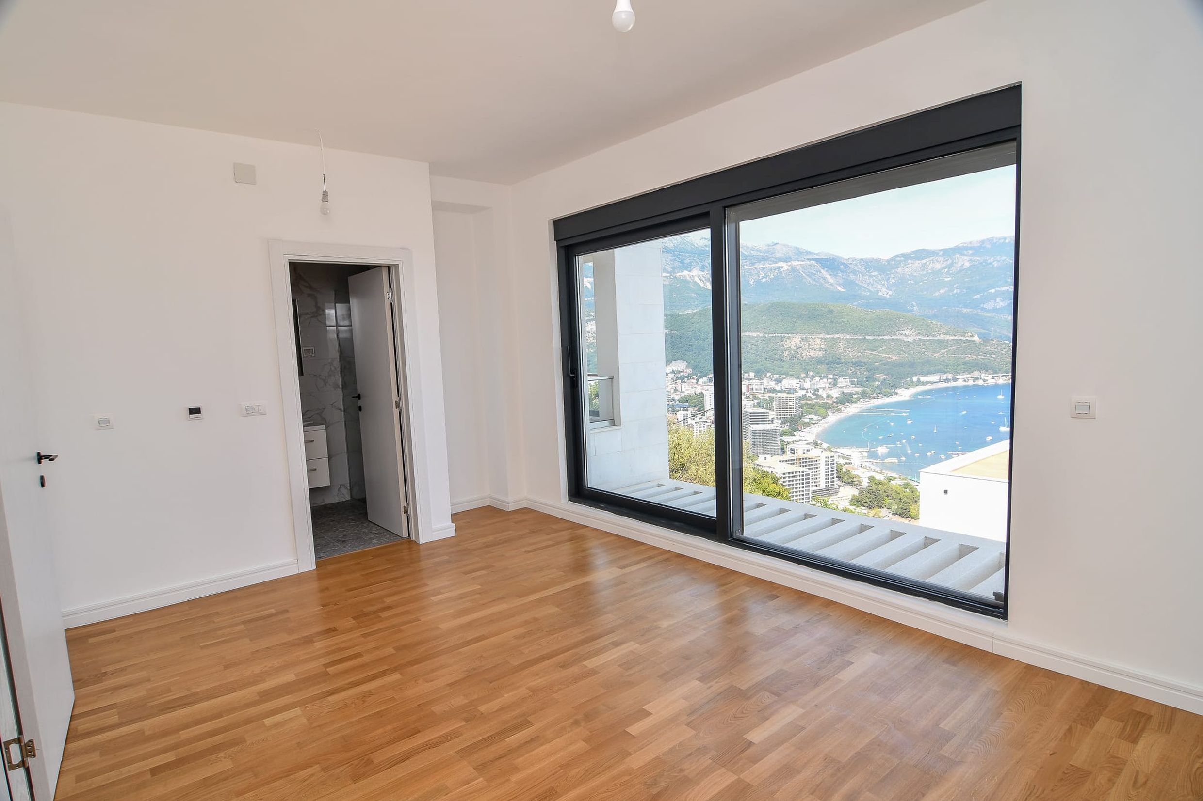 Helles Wohnzimmer mit Panoramablick auf das Meer und die Berge in einer Villa, Budva, Montenegro: Parkettboden und Zugang zur Terrasse.