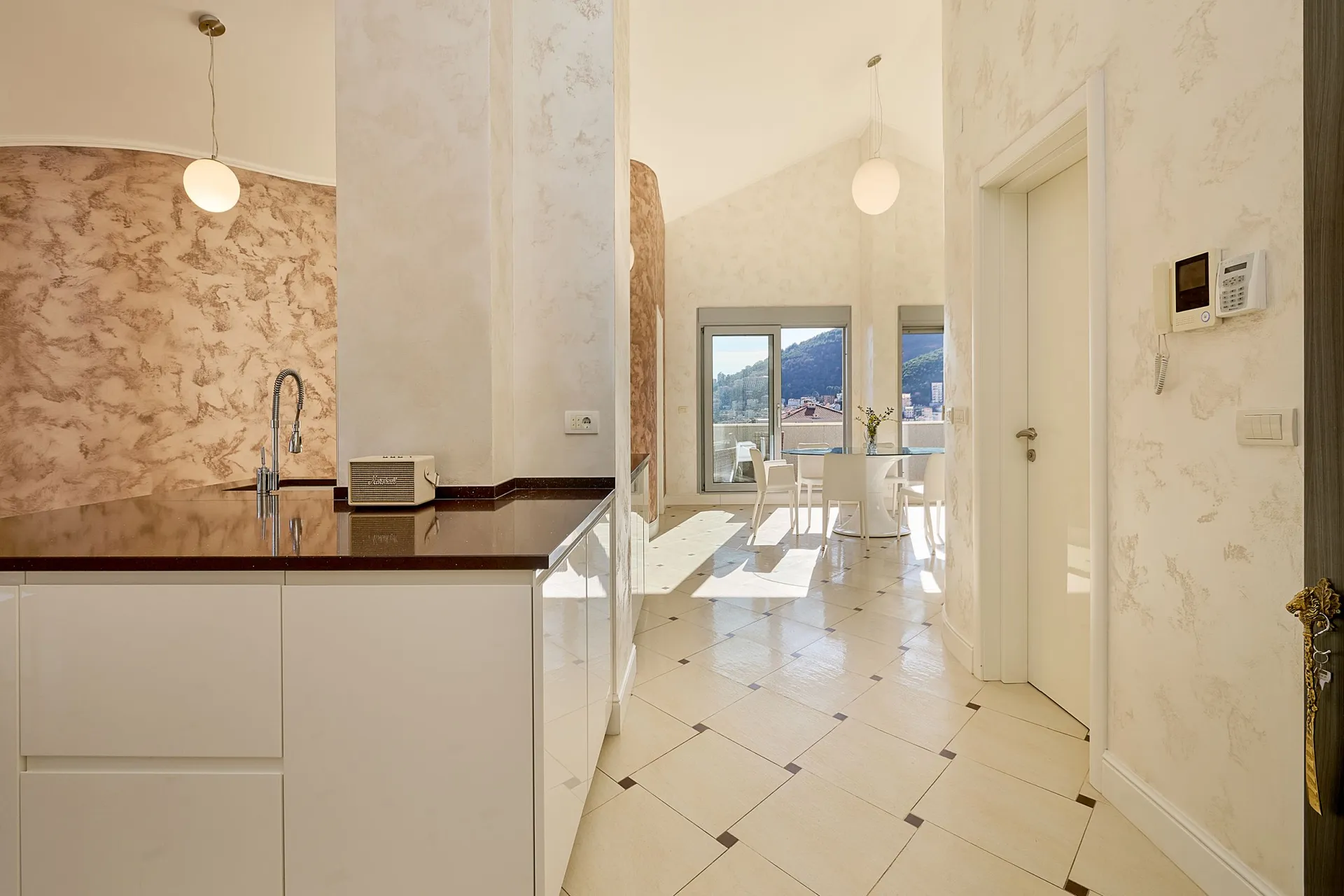 Moderne Küche mit weißen Schränken, dunkler Arbeitsplatte und dekorativer Wand. Im Hintergrund ist ein Essbereich sichtbar.