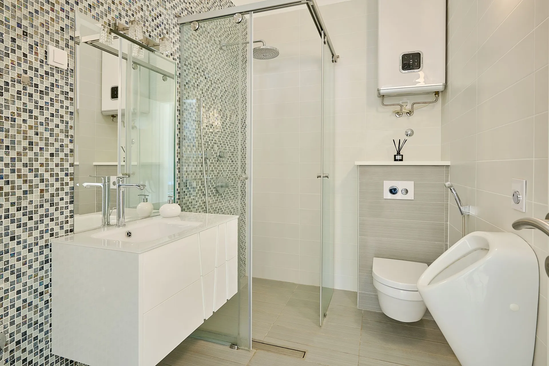 Moderne Badezimmer mit Mosaikwand, Glasdusche, weißem Waschtisch und Toilettenanlage.