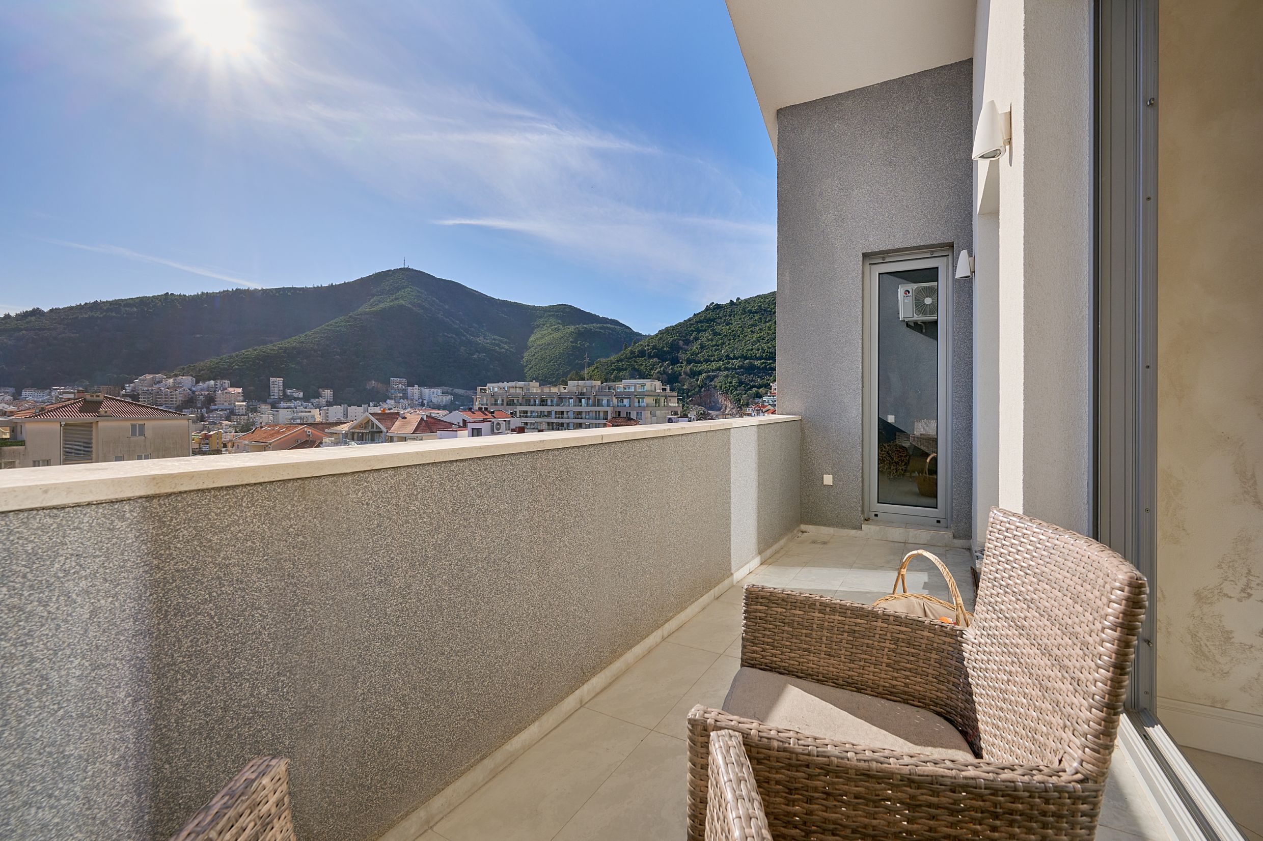 Prostran balkon sa pletenim nameštajem i panoramskim pogledom na planine i grad Budvu, Crna Gora.