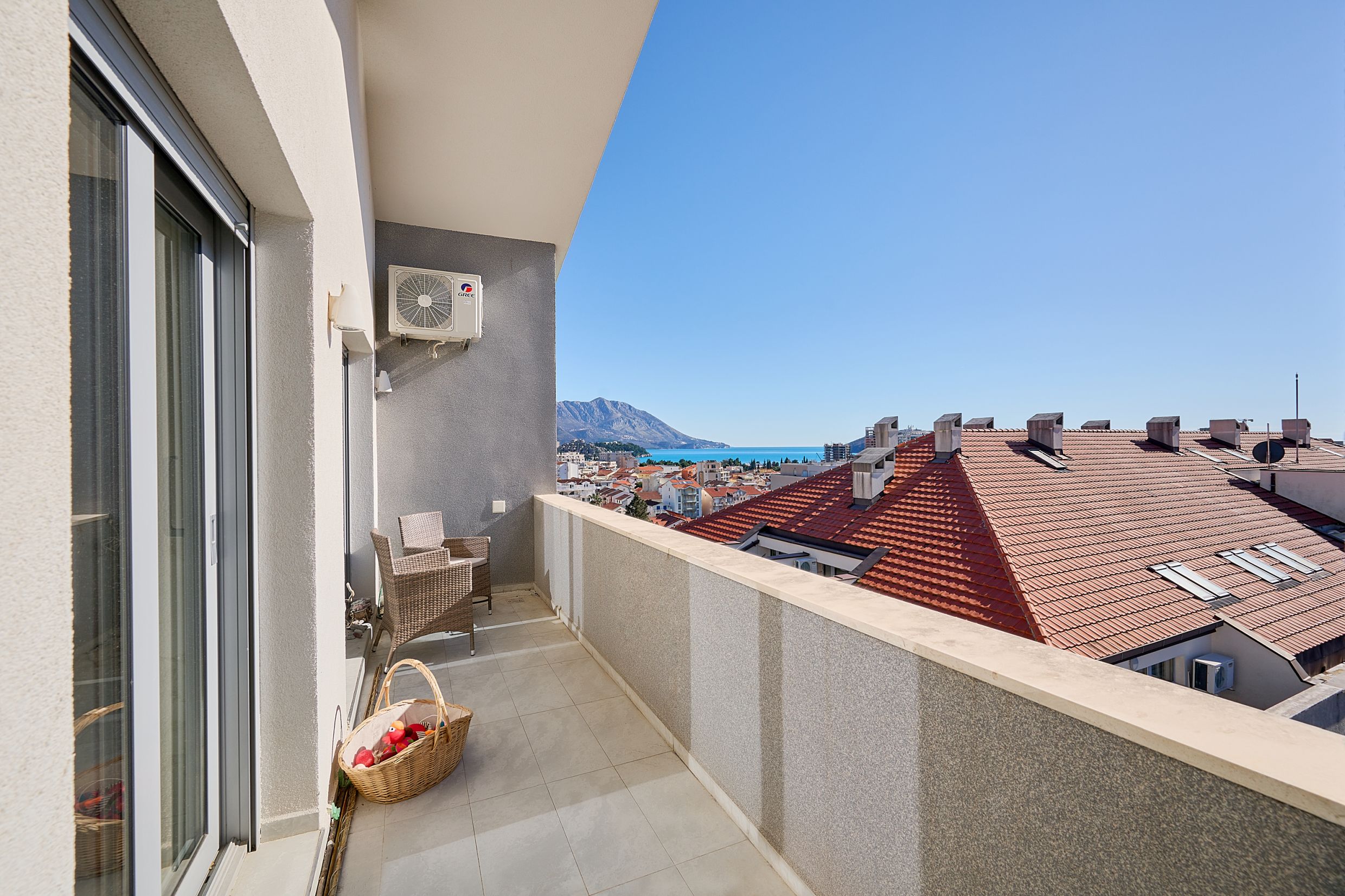 Balkon stana u Budvi, Crna Gora: pletena garnitura, pogled na more, planine i krovove grada od crepova.