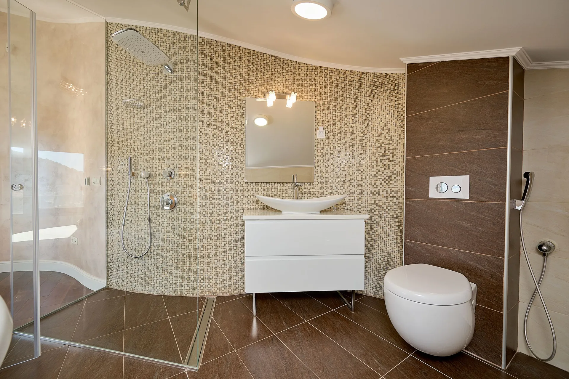 Moderne Bader mit mosaikverkleideter Dusche, weißem Waschtisch und wandmontierter Toilette.