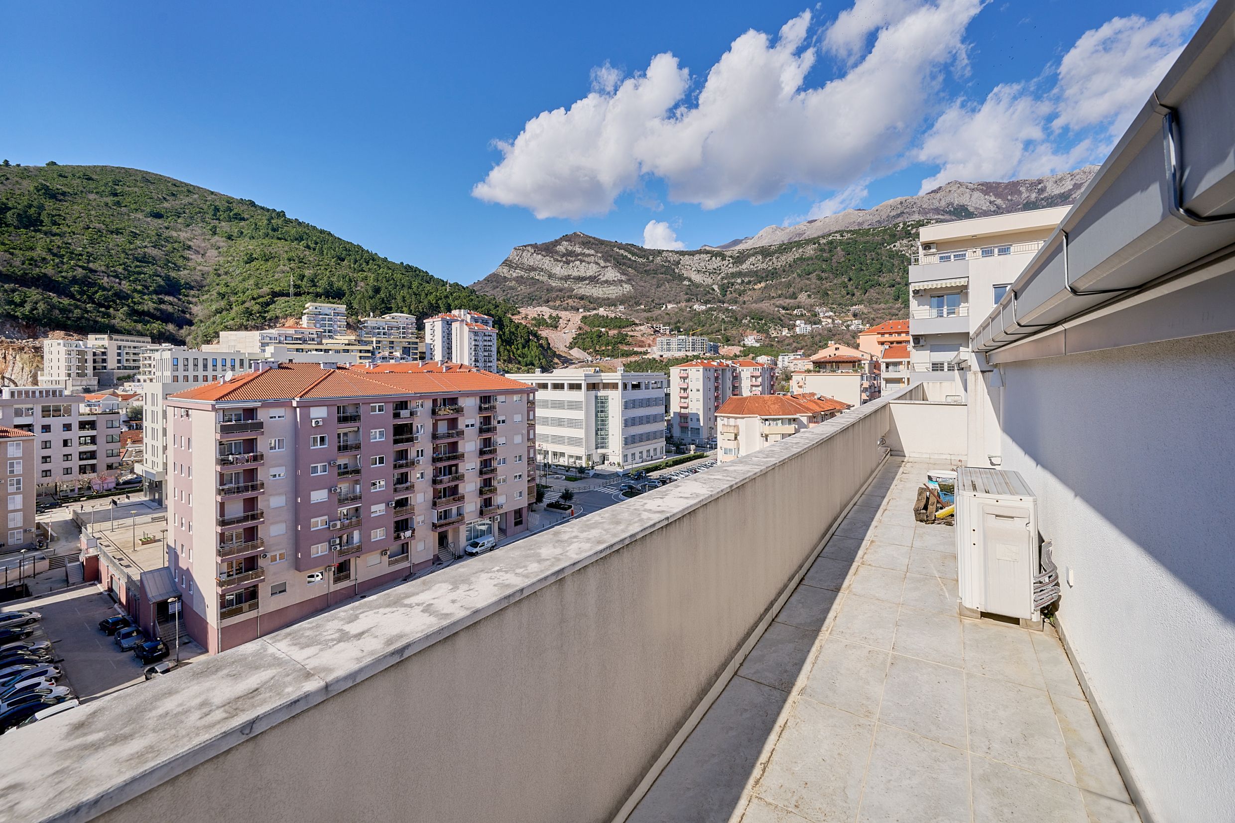 Prostran balkon stana u Budvi, Crna Gora, sa panoramskim pogledom na gradske kuće i planinski pejzaž.