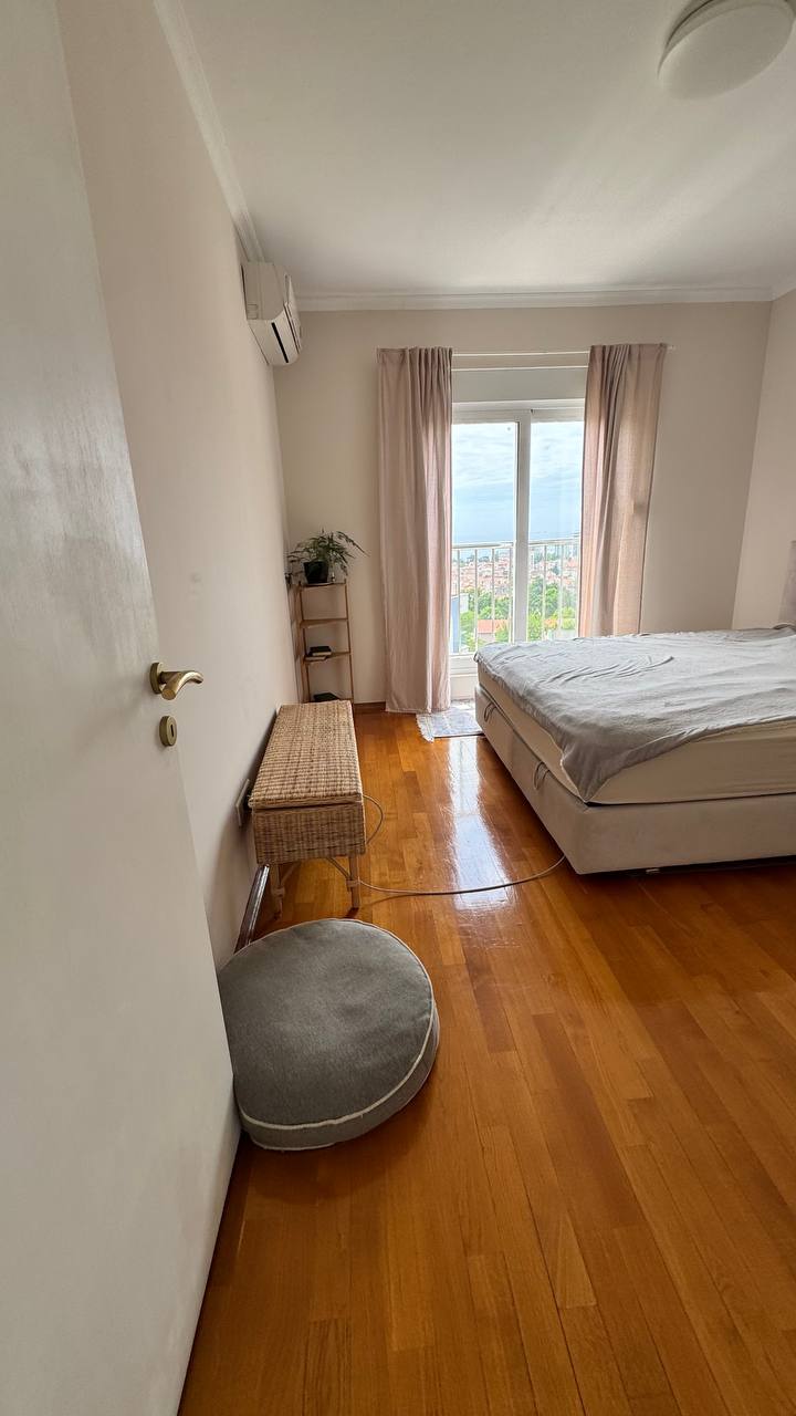 Udobna spavaća soba sa bračnim krevetom i parketom u stanu u Budvi, Crna Gora, sa izlazom na balkon i pogledom na grad.