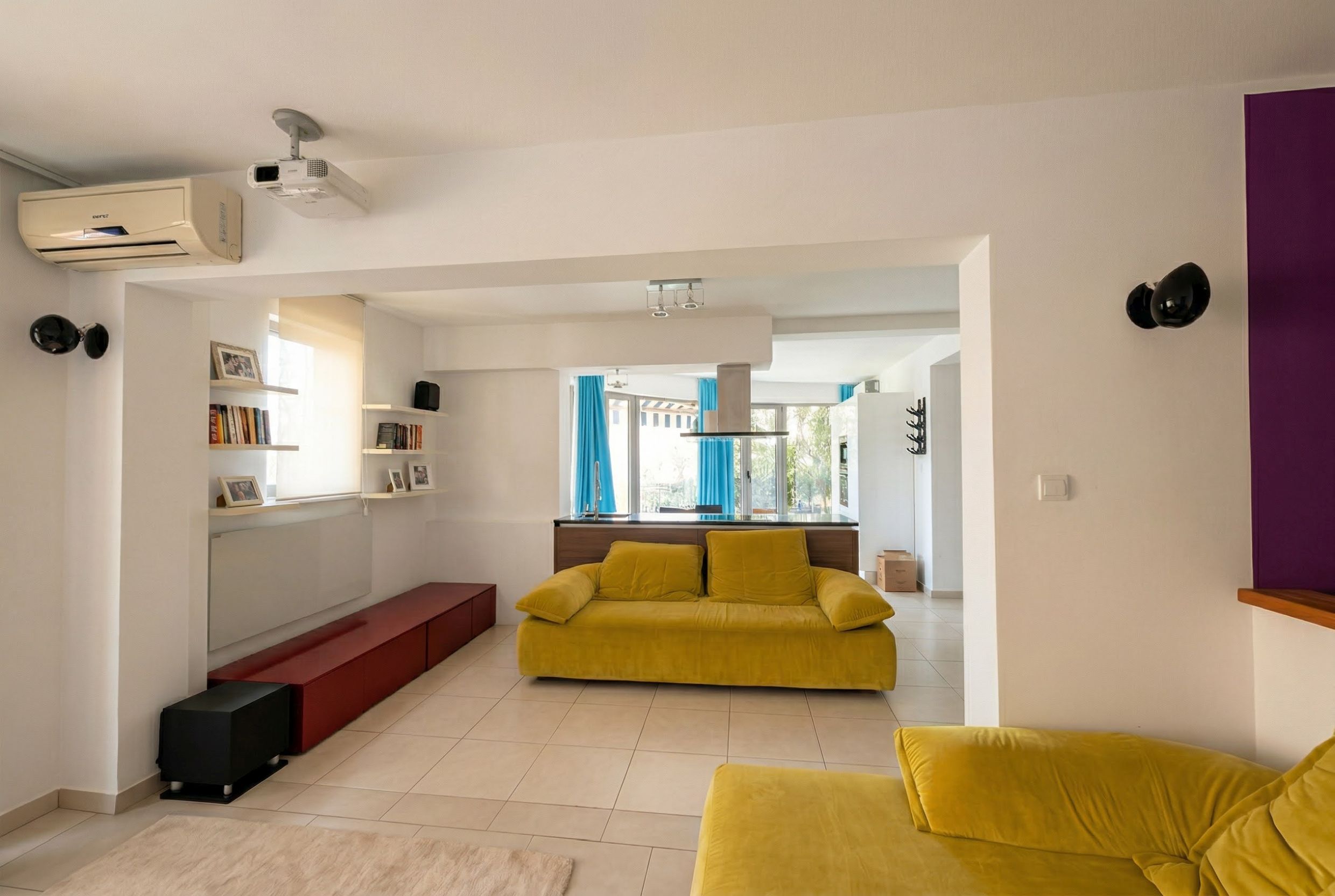 Wohnzimmer mit gelbem Sofa und Küche in einer Wohnung in Bečići, Montenegro: modernes Interieur mit Projektor und Klimaanlage.