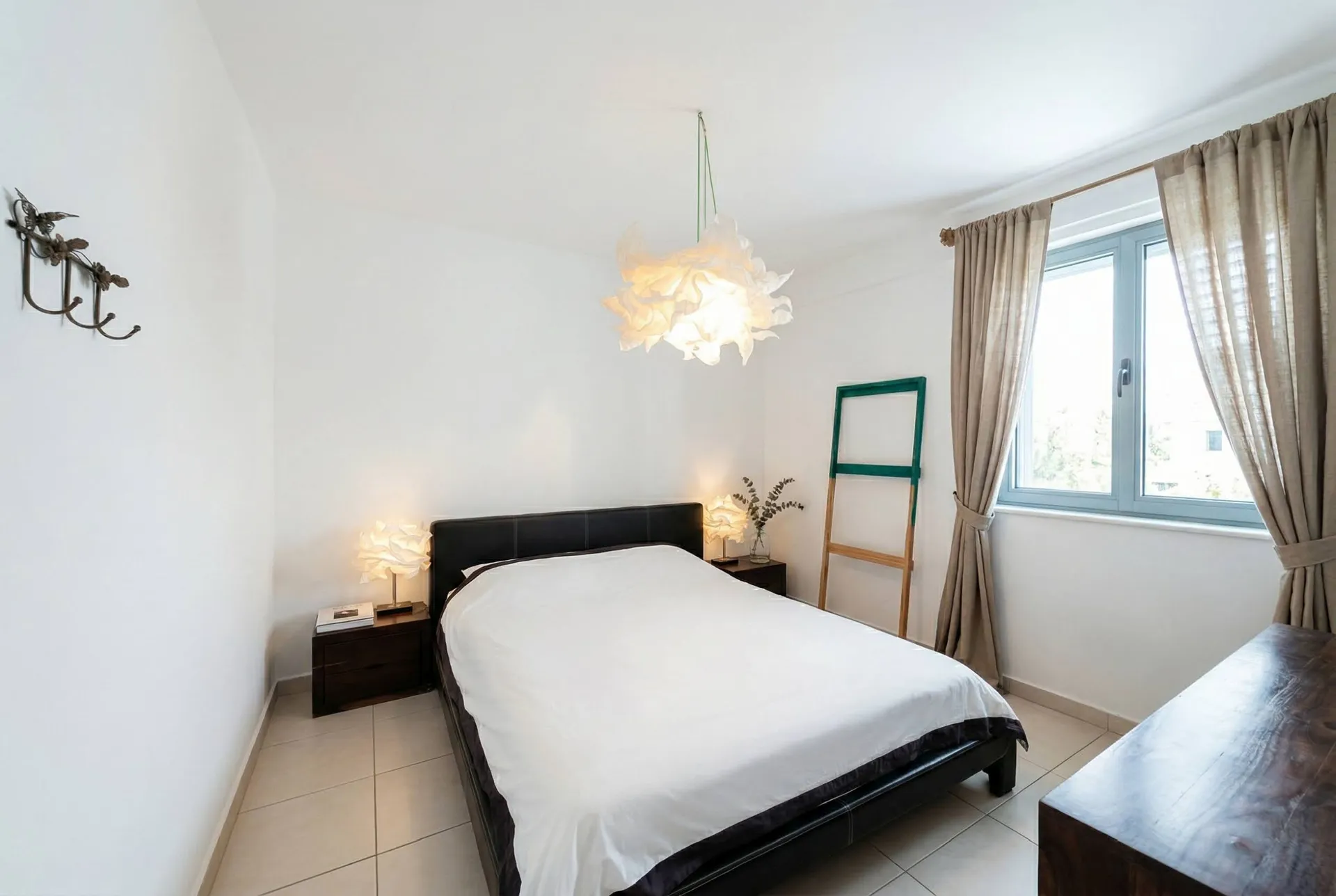 Bright bedroom featuring a double bed with white linens, dark wood nightstands, and a unique flower-shaped pendant light.