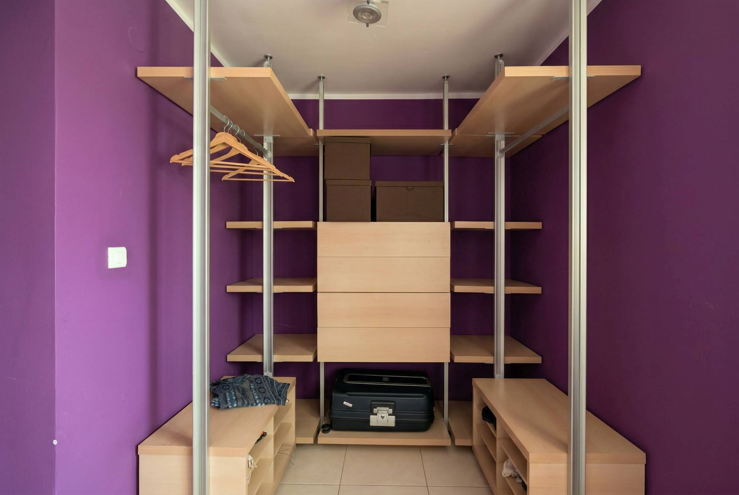 Geräumiger begehbarer Kleiderschrank mit Holzregalen und violetten Wänden in einer Wohnung, Bečići, Montenegro.