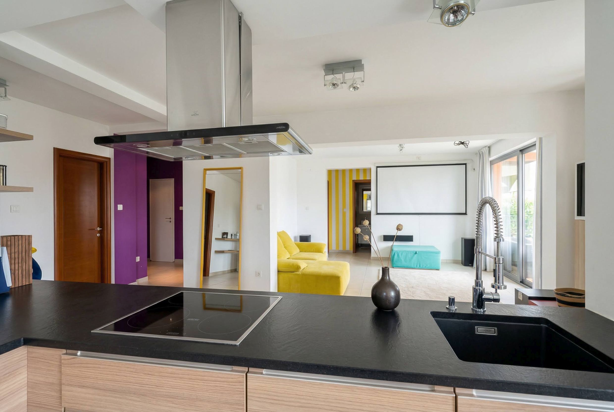 Moderne Wohnküche in einer Wohnung in Bečići, Montenegro: schwarze Arbeitsplatte, farbenfrohe Möbel und ein Projektor für Filme.