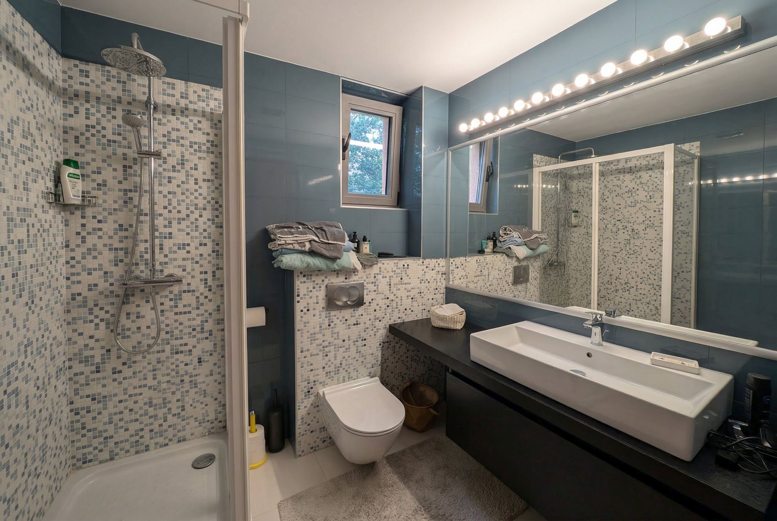 Modernes Badezimmer in einer Wohnung in Bečići, Montenegro: Duschkabine, Mosaikfliesen und hängende Sanitärkeramik.