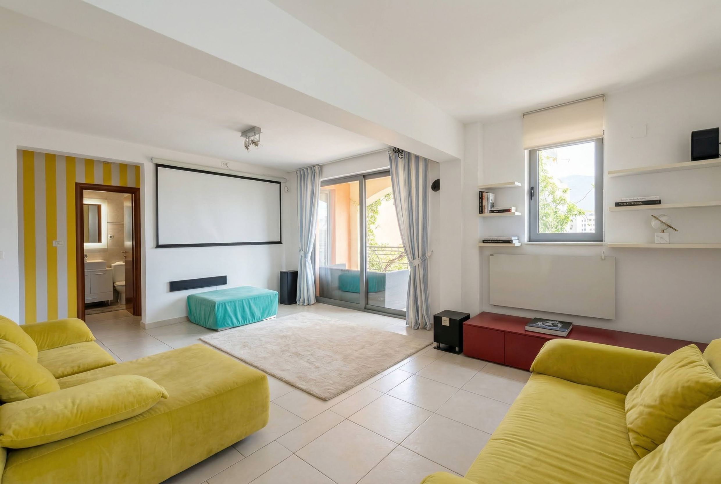 Helles Wohnzimmer mit Projektor und gelben Sofas in einer Wohnung in Bečići, Montenegro. Zugang zur Terrasse und Blick auf den Garten.