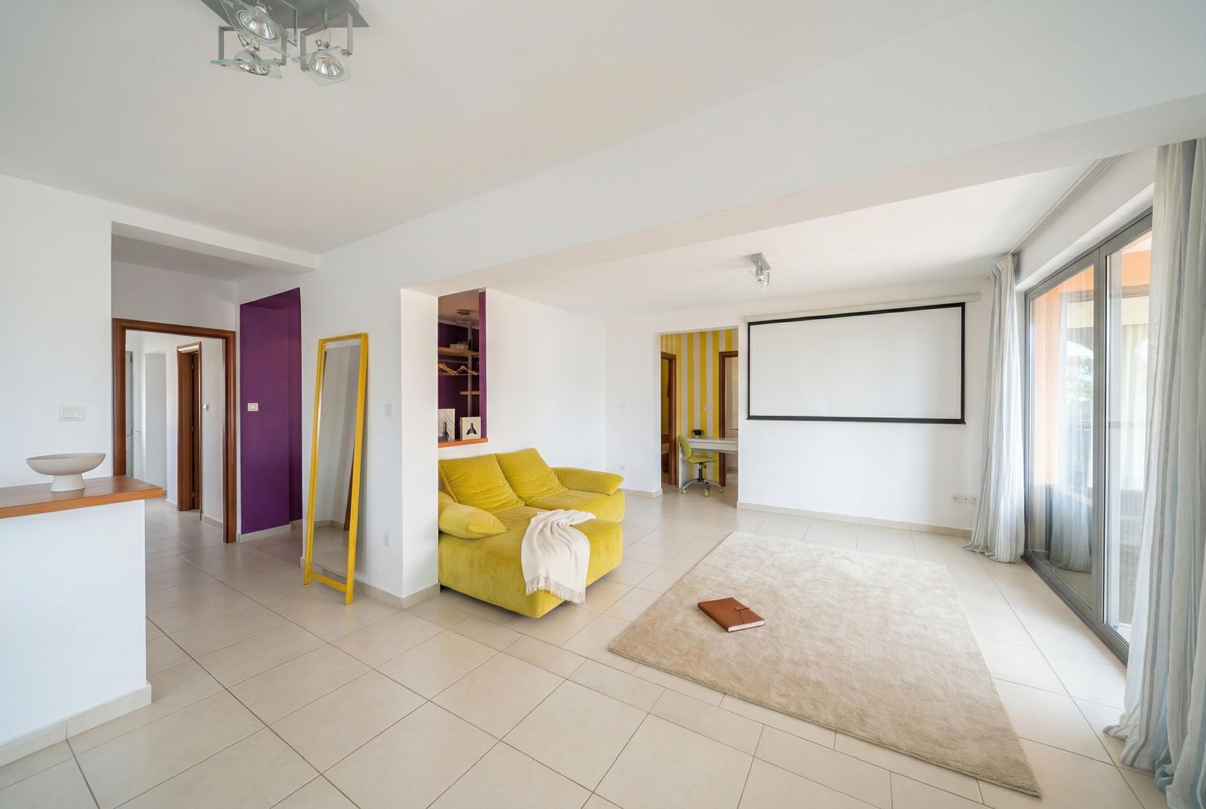 Helles Wohnzimmer mit gelbem Sofa und Projektor in einer Wohnung, Bečići, Montenegro. Modernes Interieur mit Panoramafenster.