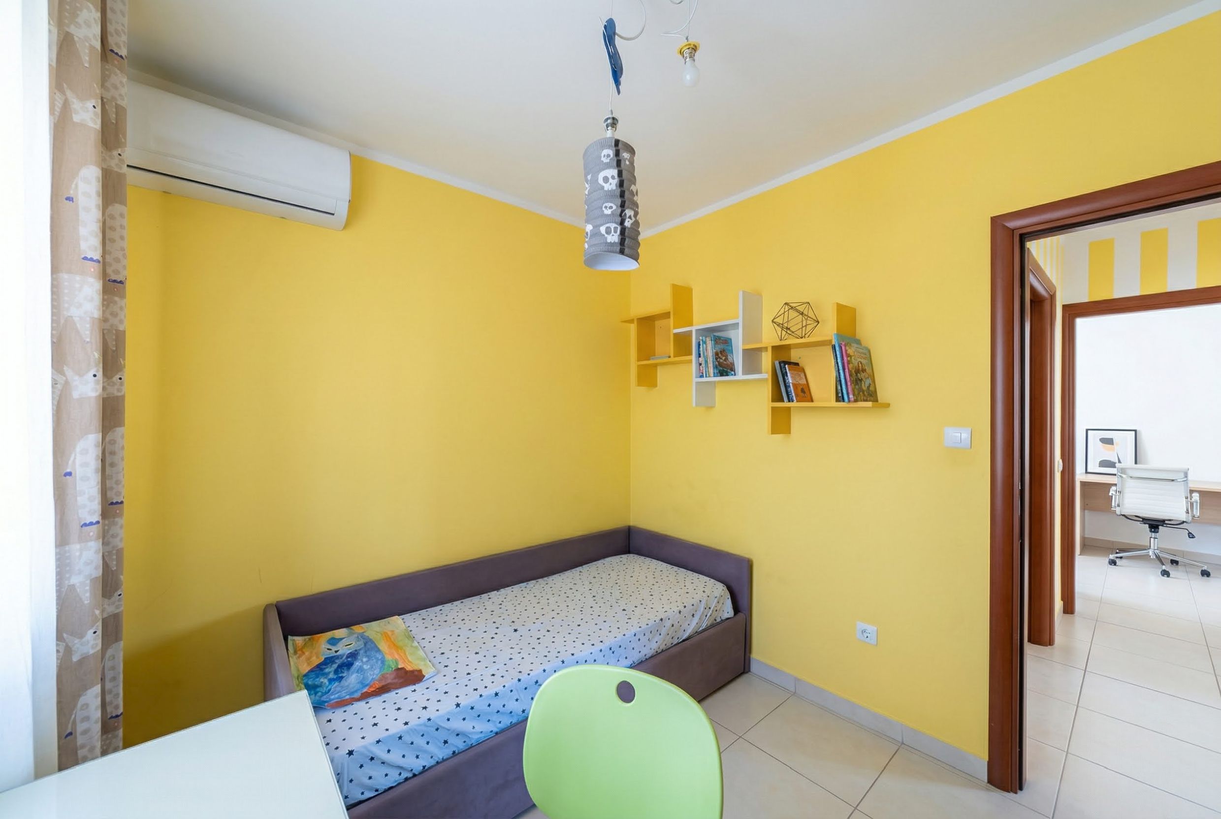 Kinderzimmer mit gelben Wänden und Bett in einer Wohnung, Bečići, Montenegro. Gemütliches Interieur mit Regalen und Klimaanlage.