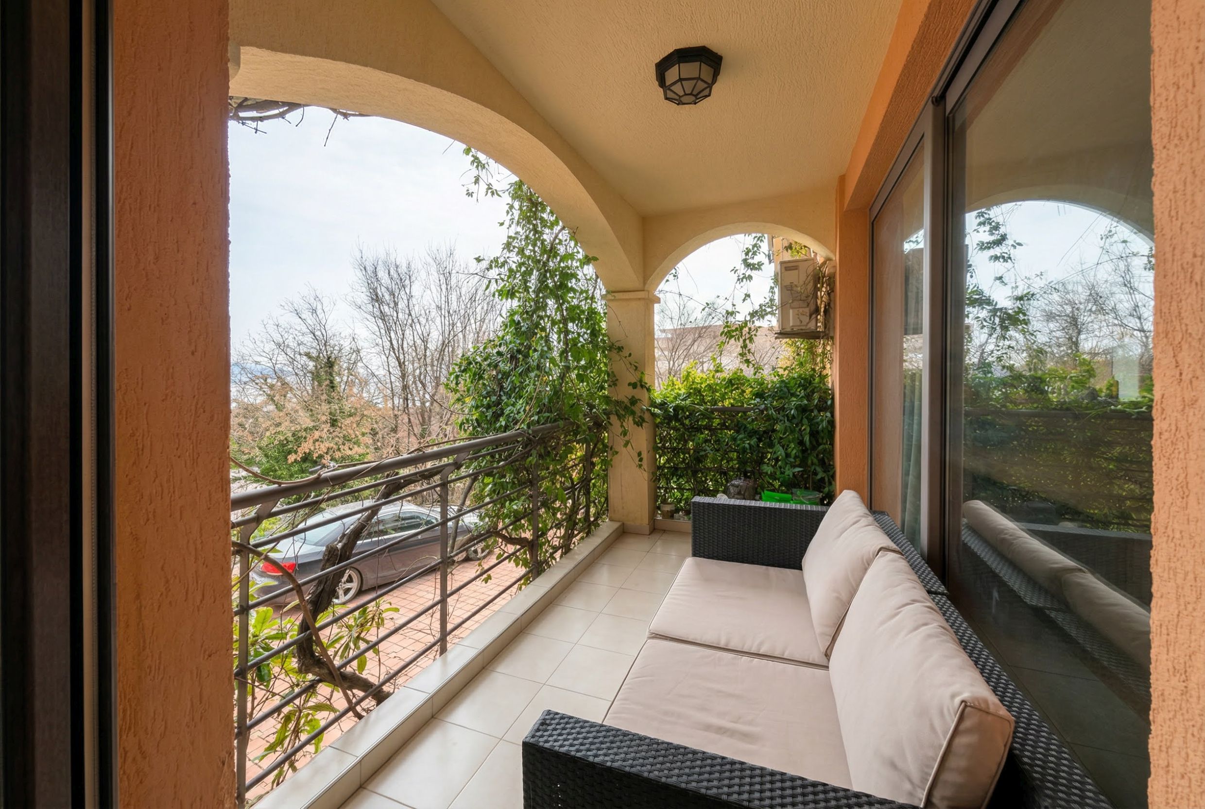 Gemütlicher Balkon mit Rattanmöbeln in einer Wohnung in Bečići, Montenegro: Blick ins Grüne und auf bogenförmige Designelemente.