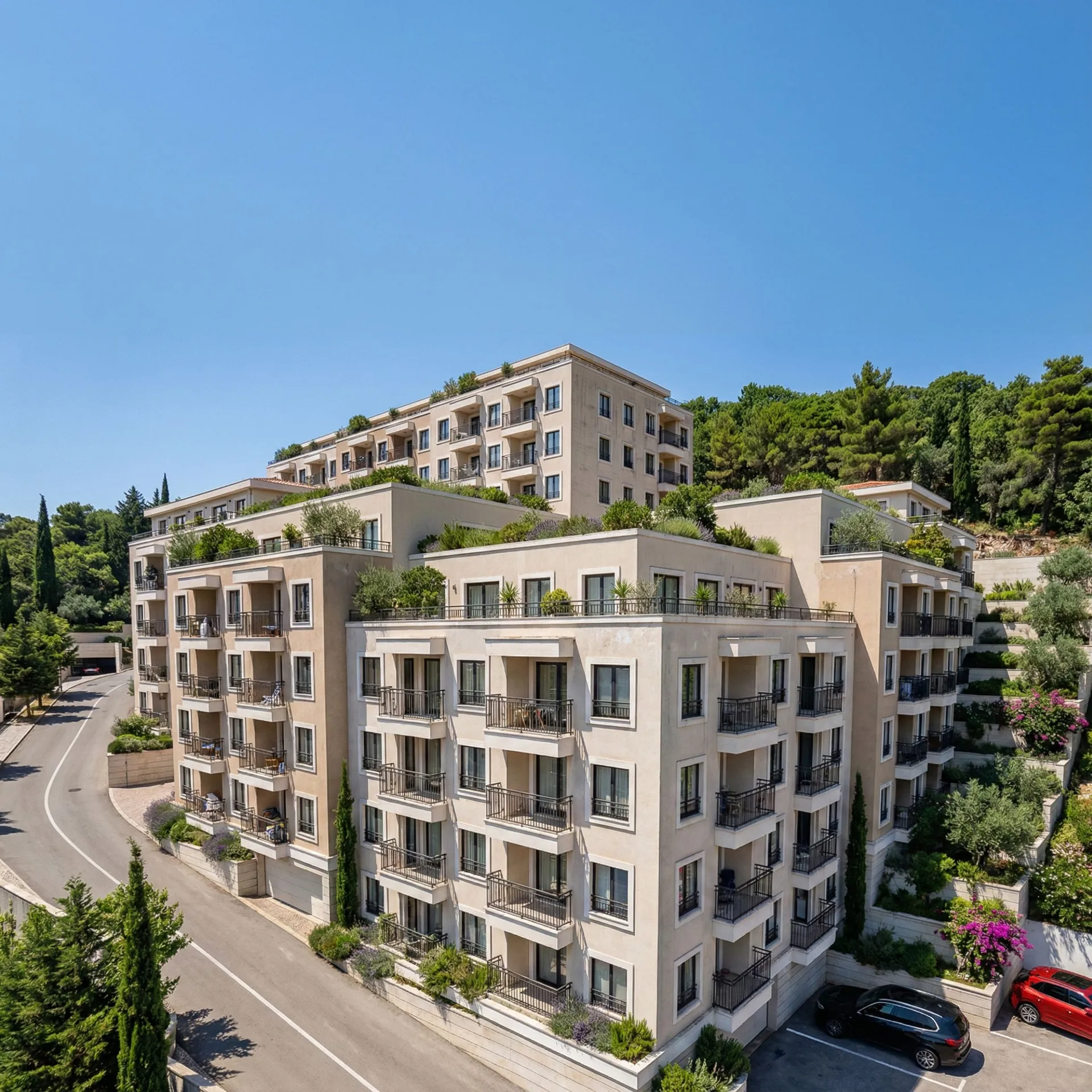 Vue aérienne d'un complexe résidentiel à plusieurs étages avec balcons et terrasses entouré de verdure sous un ciel clair.