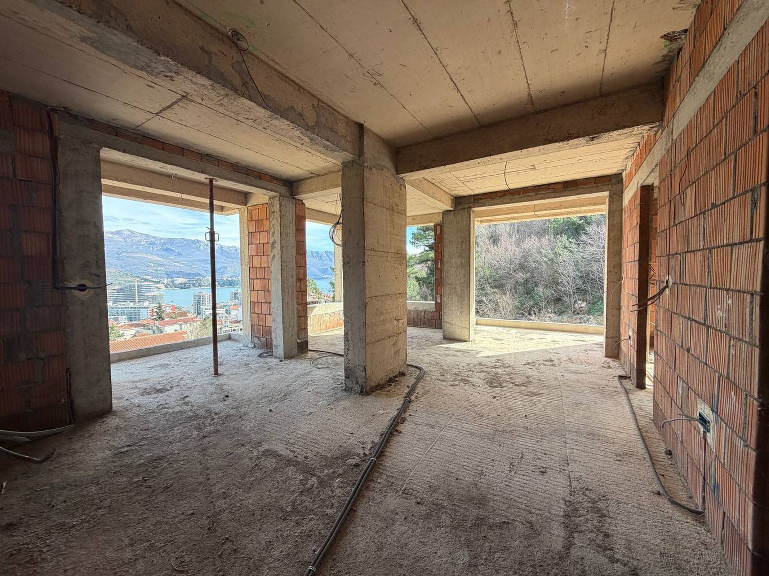 Dnevna soba bez završne obrade u stambenom kompleksu u izgradnji u Budvi, Crna Gora, sa panoramskim pogledom na more i planine.