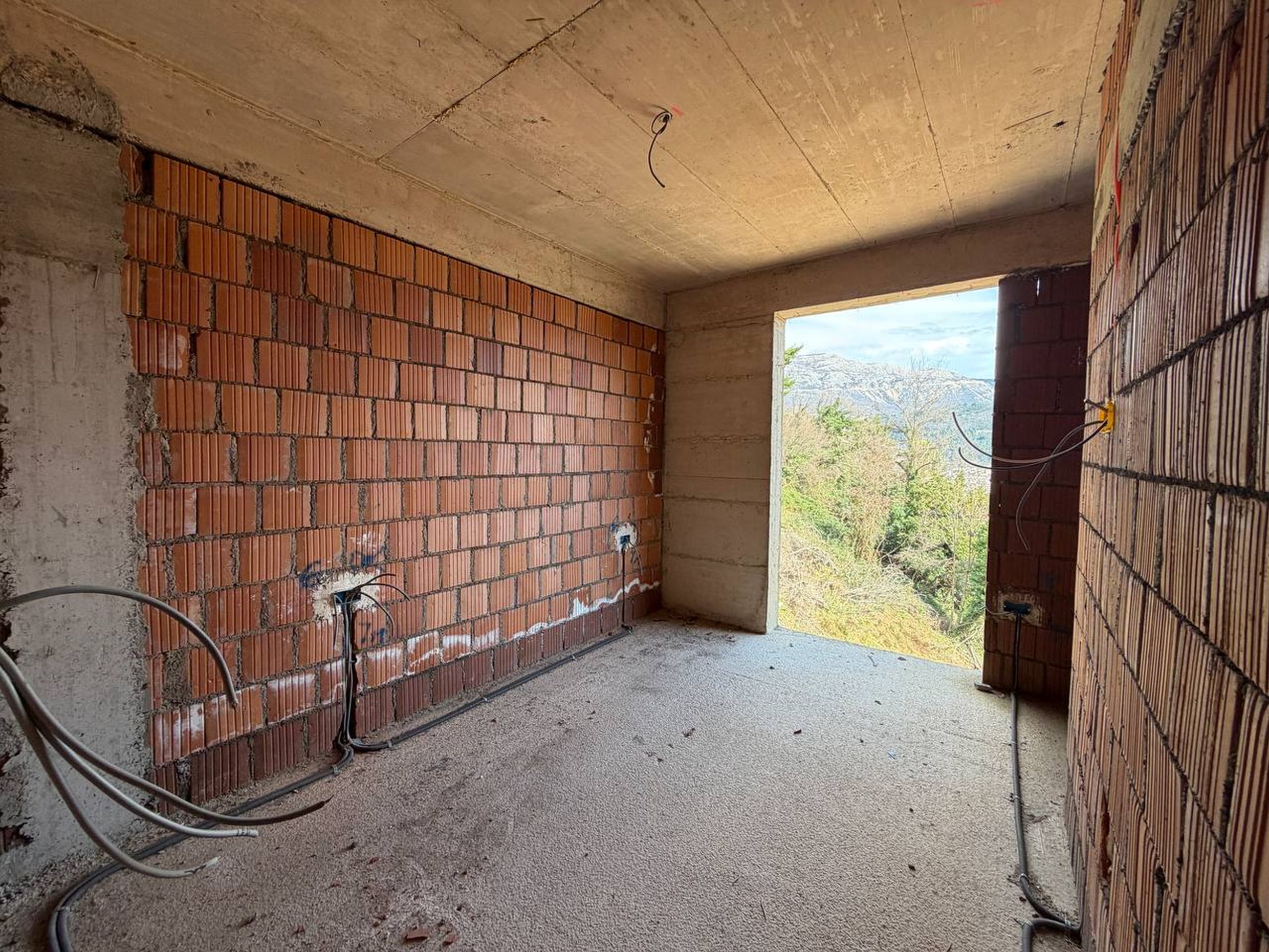 Grubi radovi u stanu u novogradnji u Budvi, Crna Gora: zidovi od cigle, betonski plafon i pogled na planine.