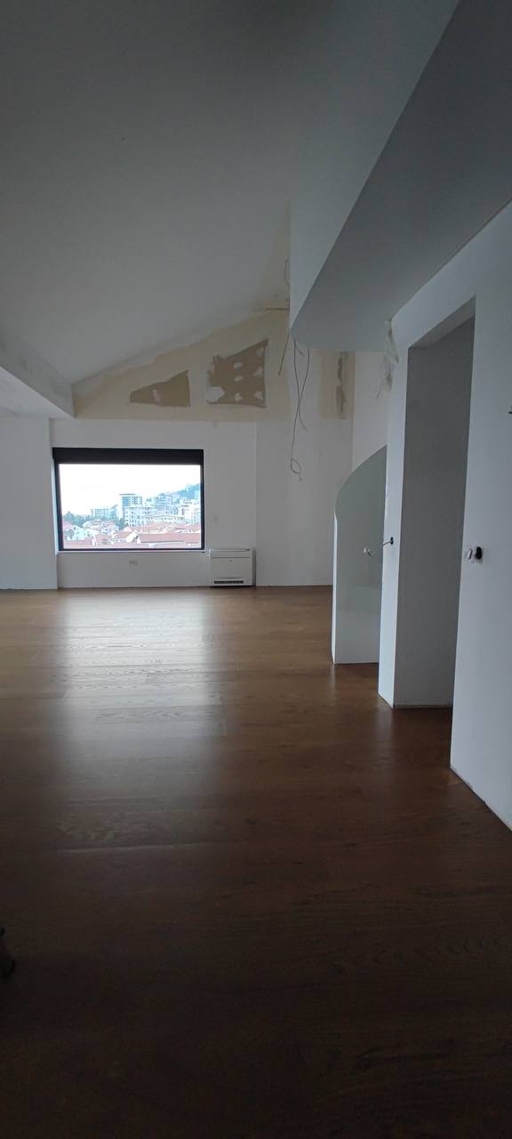 Geräumiges Wohnzimmer in einem Penthouse in Budva, Montenegro: helle Ausstattung, Holzboden und Panoramablick auf die Stadt.