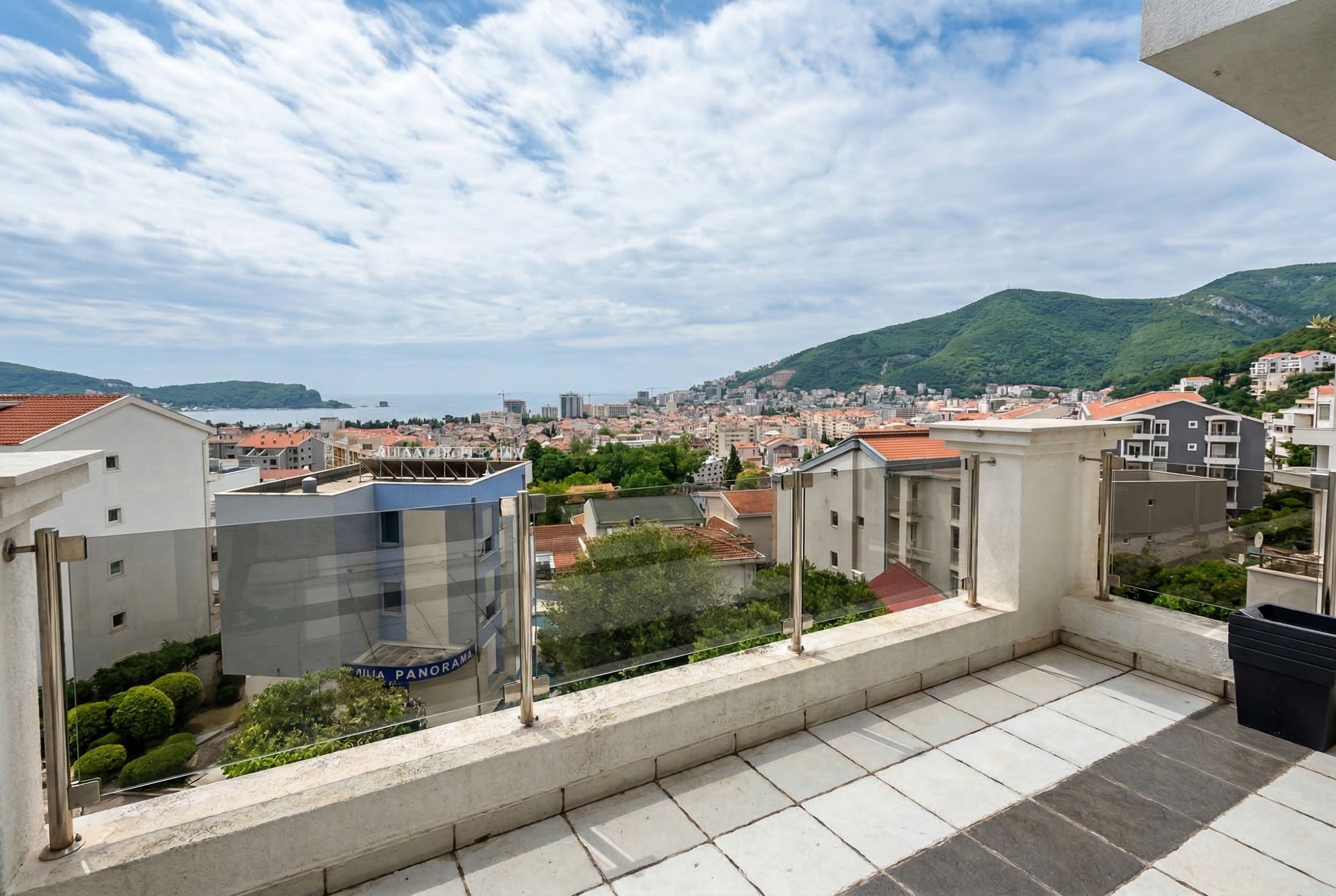 Panoramski pogled na more i planine sa balkona stana u Budvi, Crna Gora, sa modernom staklenom ogradom.