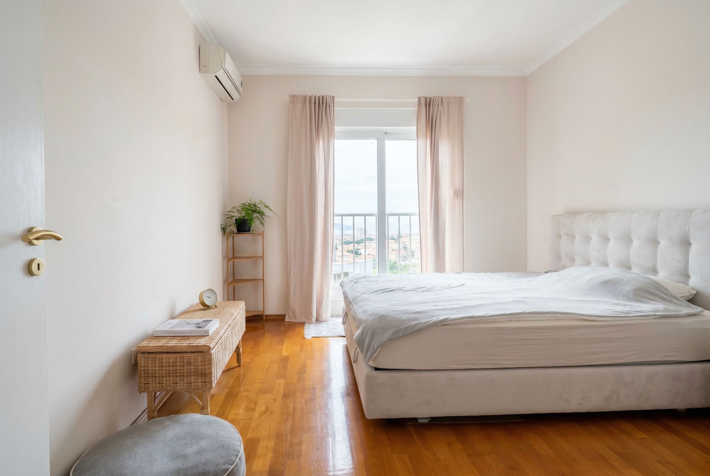 Svetla spavaća soba sa bračnim krevetom, parketom i izlazom na balkon u stanu u Budvi, Crna Gora.