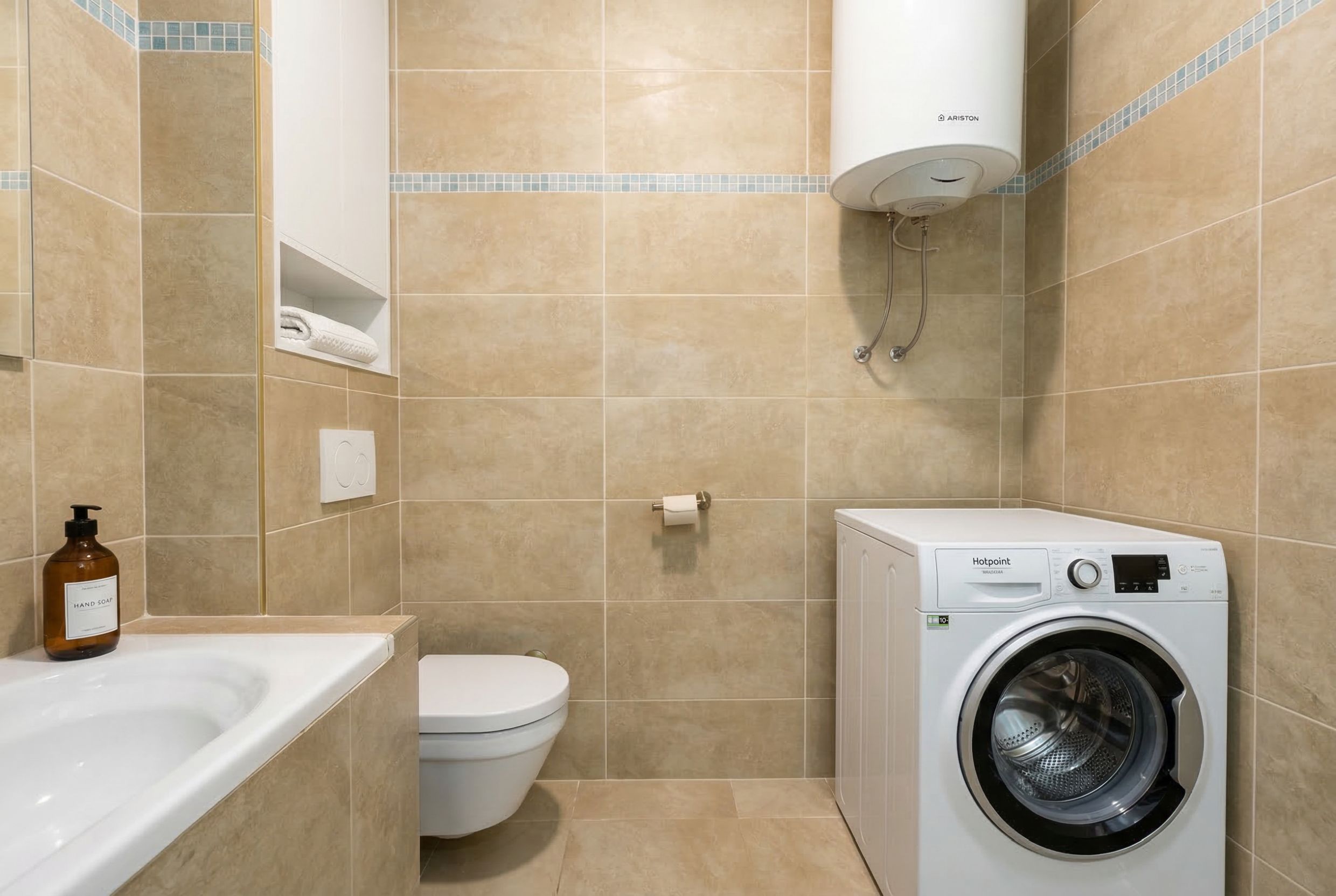 Kupatilo u stanu u Budvi, Crna Gora: bež pločice, veš mašina Hotpoint, bojler Ariston i sanitarije.