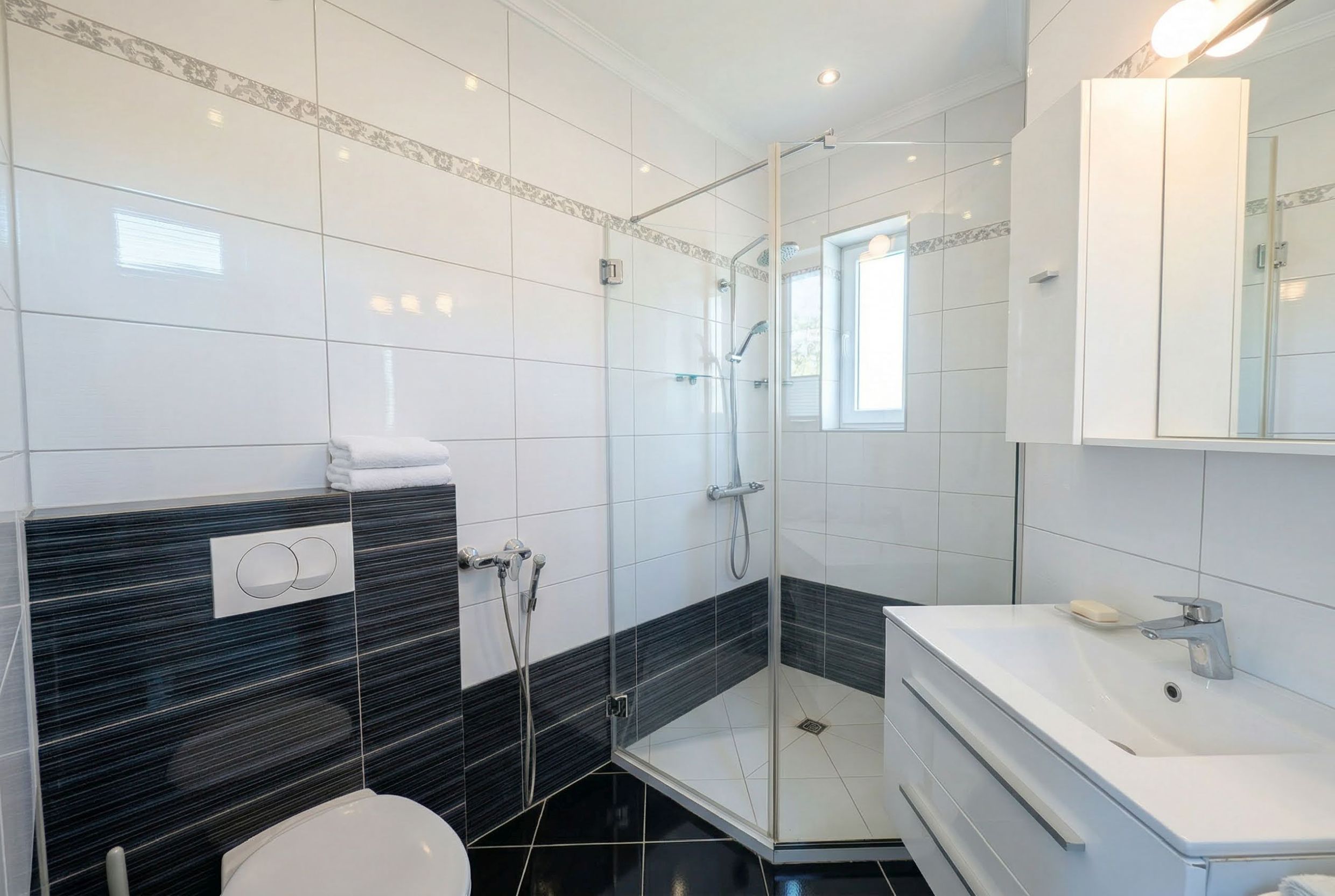 Modern bathroom in an apartment in Bečići, Montenegro: shower cabin, white sanitary ware, and black-and-white tiles.
