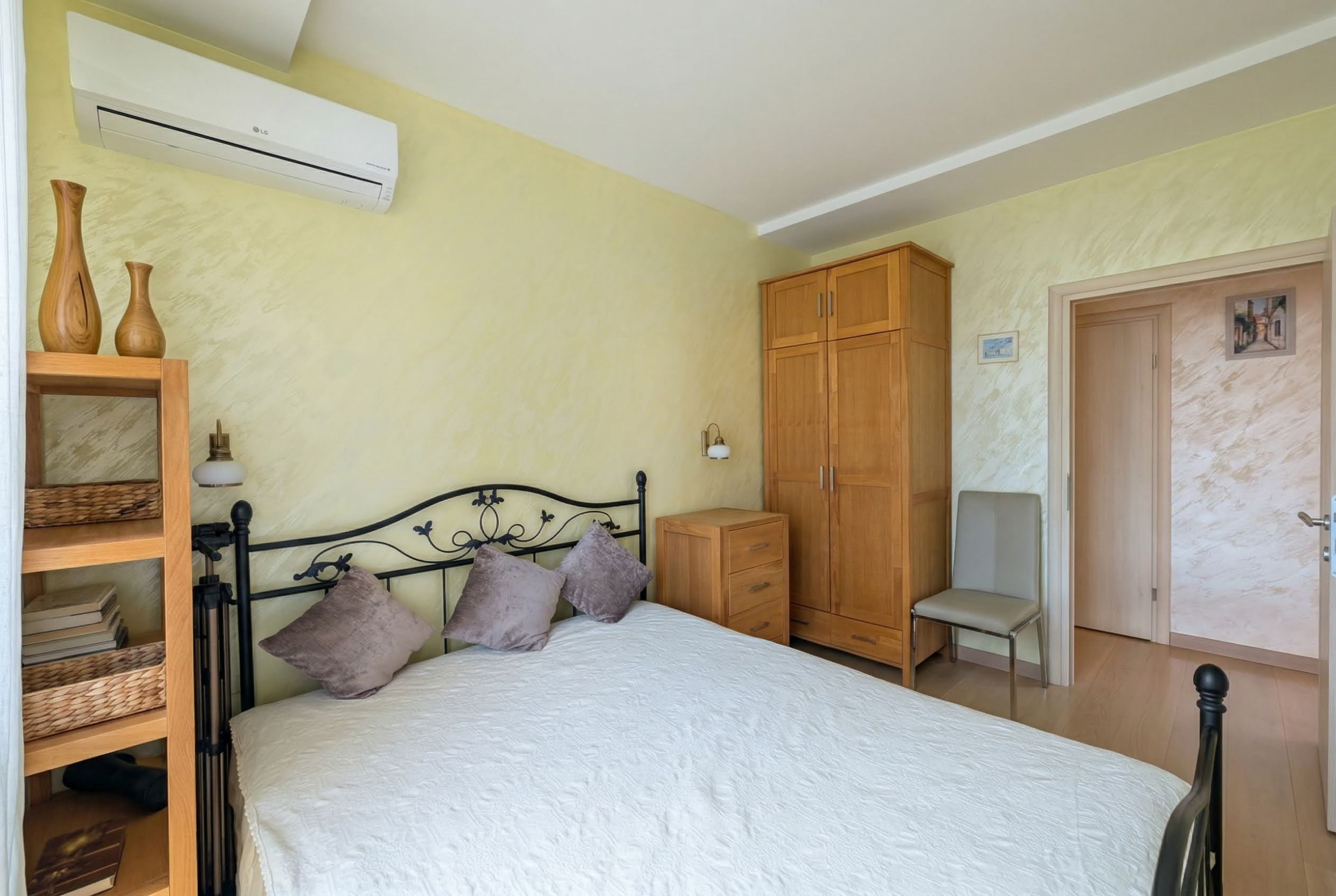 Cozy bedroom with a wrought-iron bed and wooden furniture in an apartment in Bečići, Montenegro. Bright interior with air conditioning.