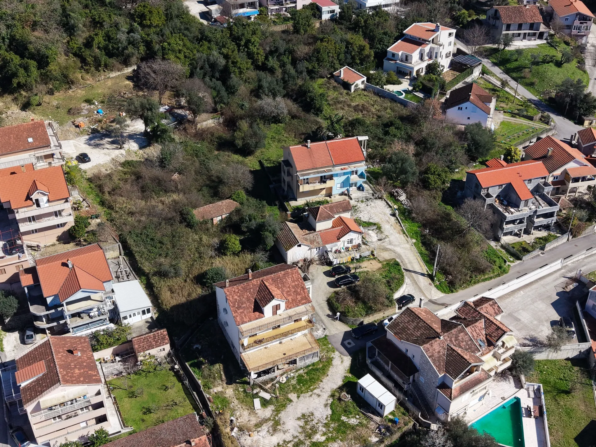 Kırmızı kiremitli evler, yeşil tepeler ve özel havuzlarla kaplı bir konut bölgesinin hava fotoğrafı.