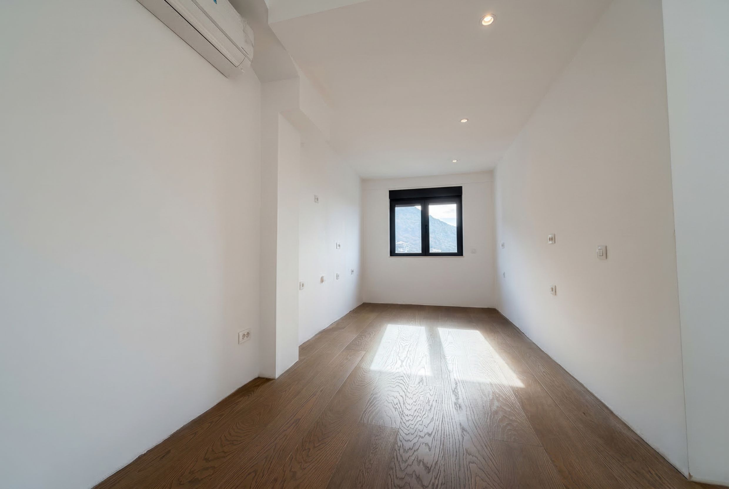 Helles, leeres Schlafzimmer mit Parkettboden und Bergblick in einem Penthouse, Budva, Montenegro. Moderne Ausstattung und Klimaanlage.