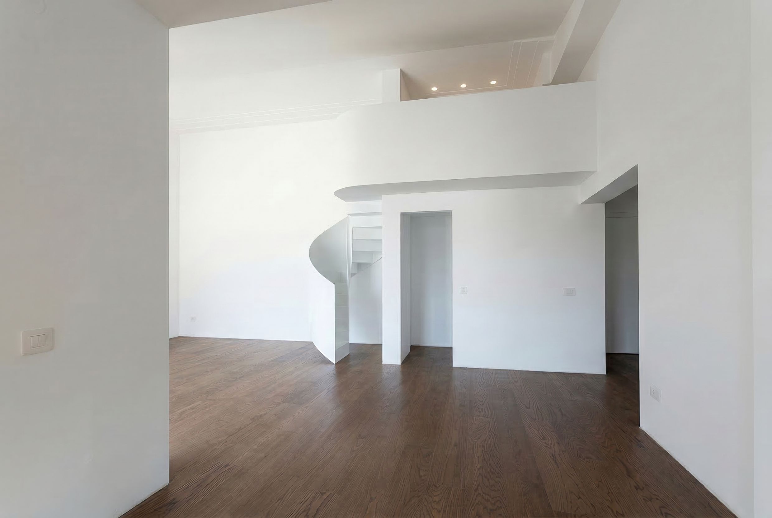 Interieur eines zweistöckigen Wohnzimmers in einem Penthouse in Budva, Montenegro: weiße Wände, Wendeltreppe und Parkettboden.