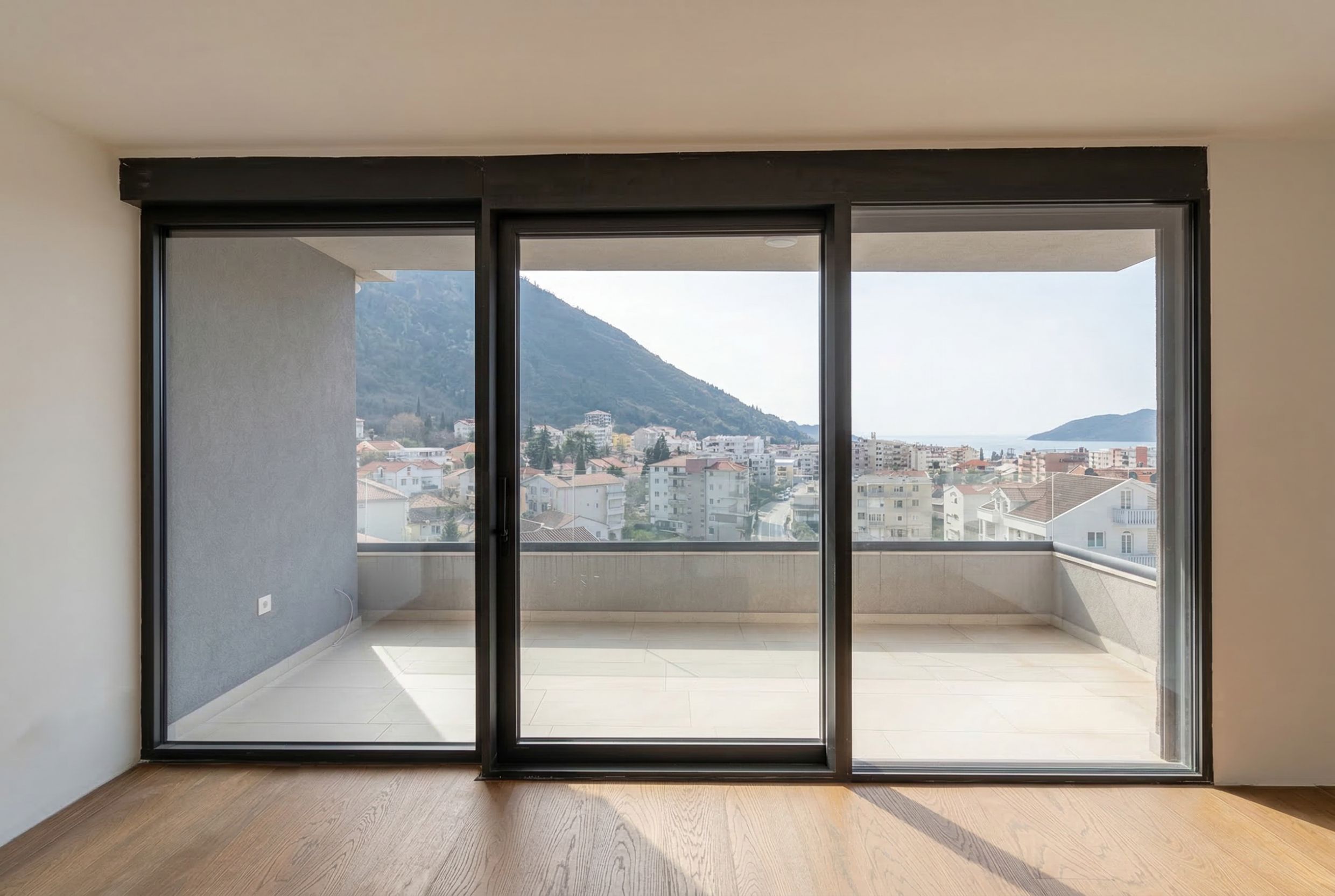 Panoramafenster im Wohnzimmer eines Penthouses in Budva, Montenegro, mit Zugang zu einer großzügigen Terrasse und Blick auf das Meer und die Berge.