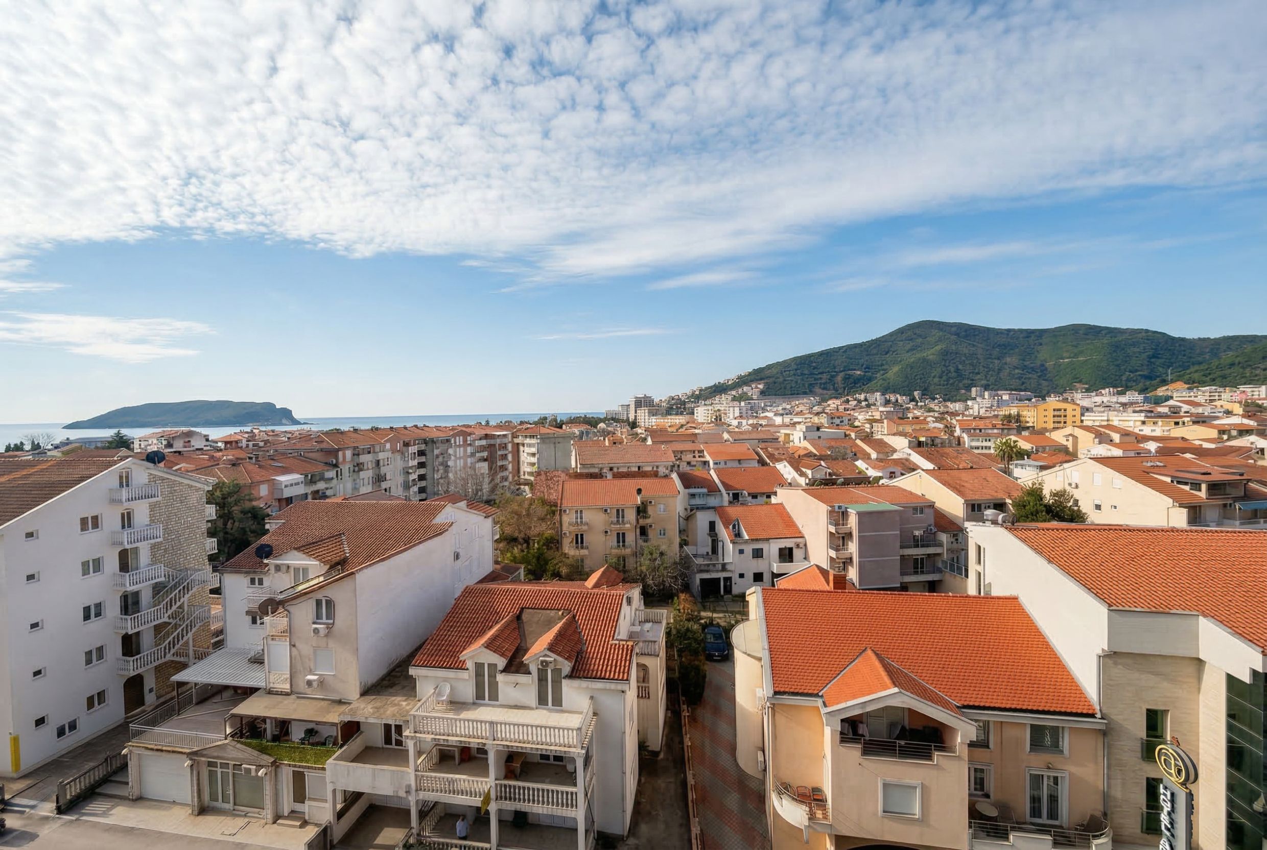 Panoramablick auf die Stadt Budva und die Adria von einem Penthouse in Montenegro mit Ziegeldächern und Bergen im Hintergrund.