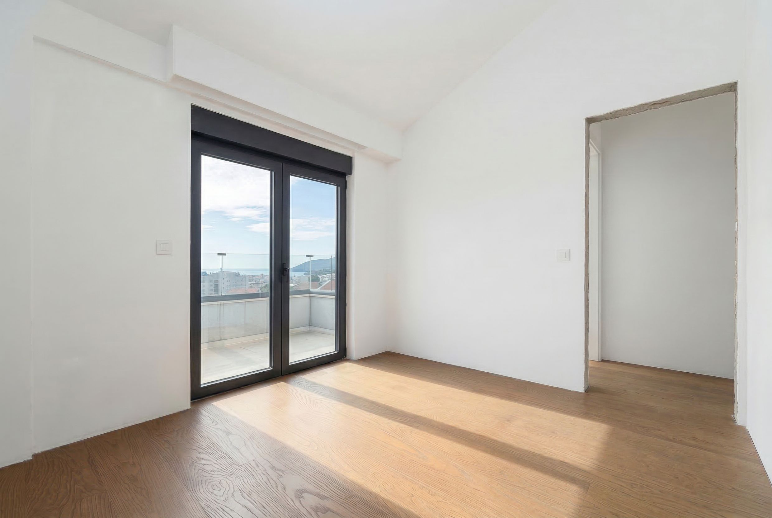 Helles Schlafzimmer in einem Penthouse in Budva, Montenegro: Panoramafenster, Zugang zum Balkon mit Meerblick, Parkettboden.