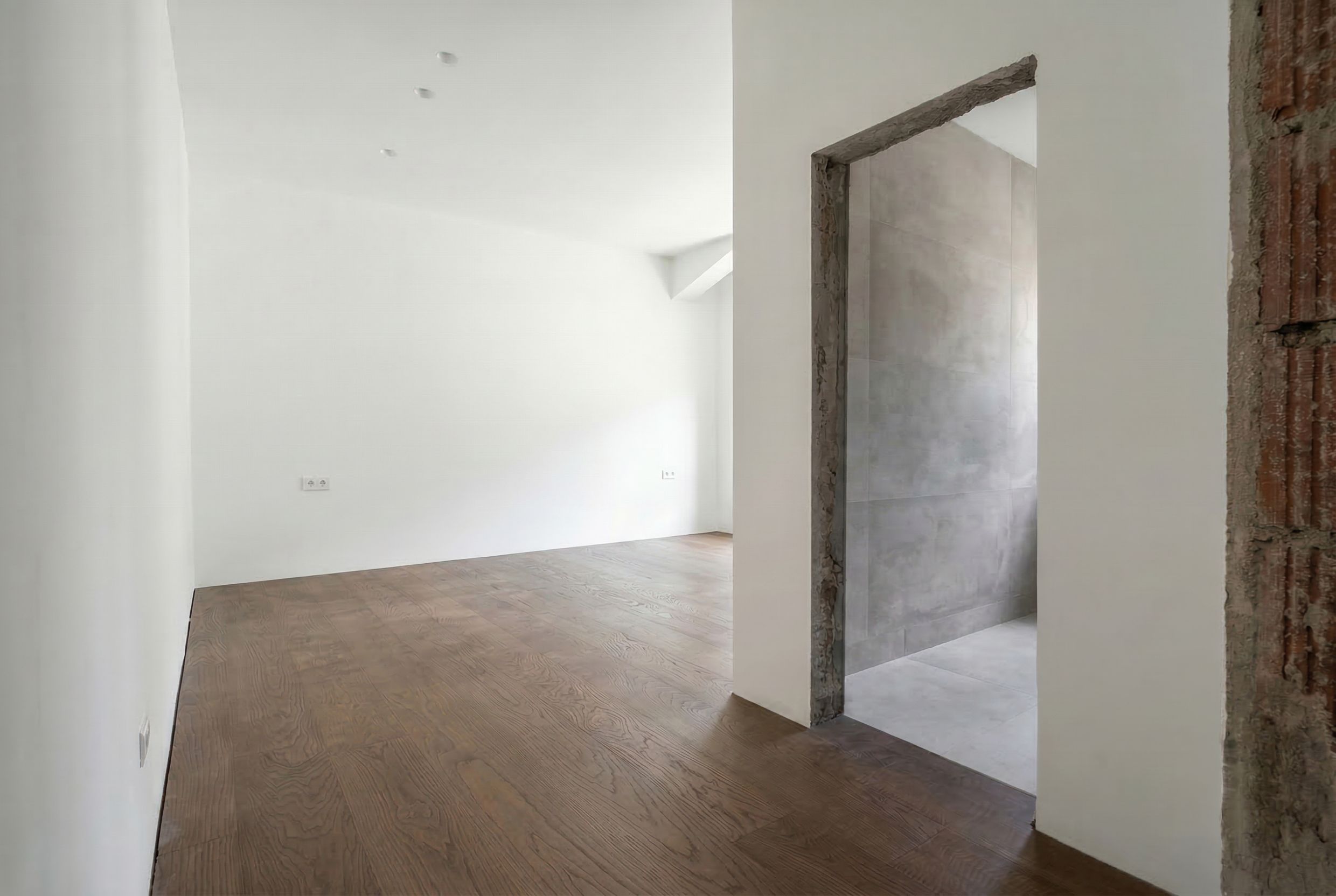 Wohnzimmerinterieur in einem Penthouse in Budva, Montenegro: helle Wände, Holzboden und Zugang zum gefliesten Badezimmer.