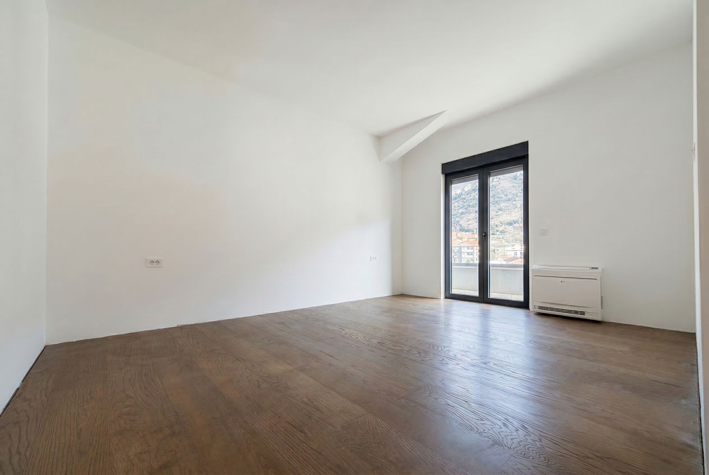Helles Wohnzimmer in einem Penthouse in Budva, Montenegro: Parkettboden, weiße Wände, Panoramatür und Bergblick.