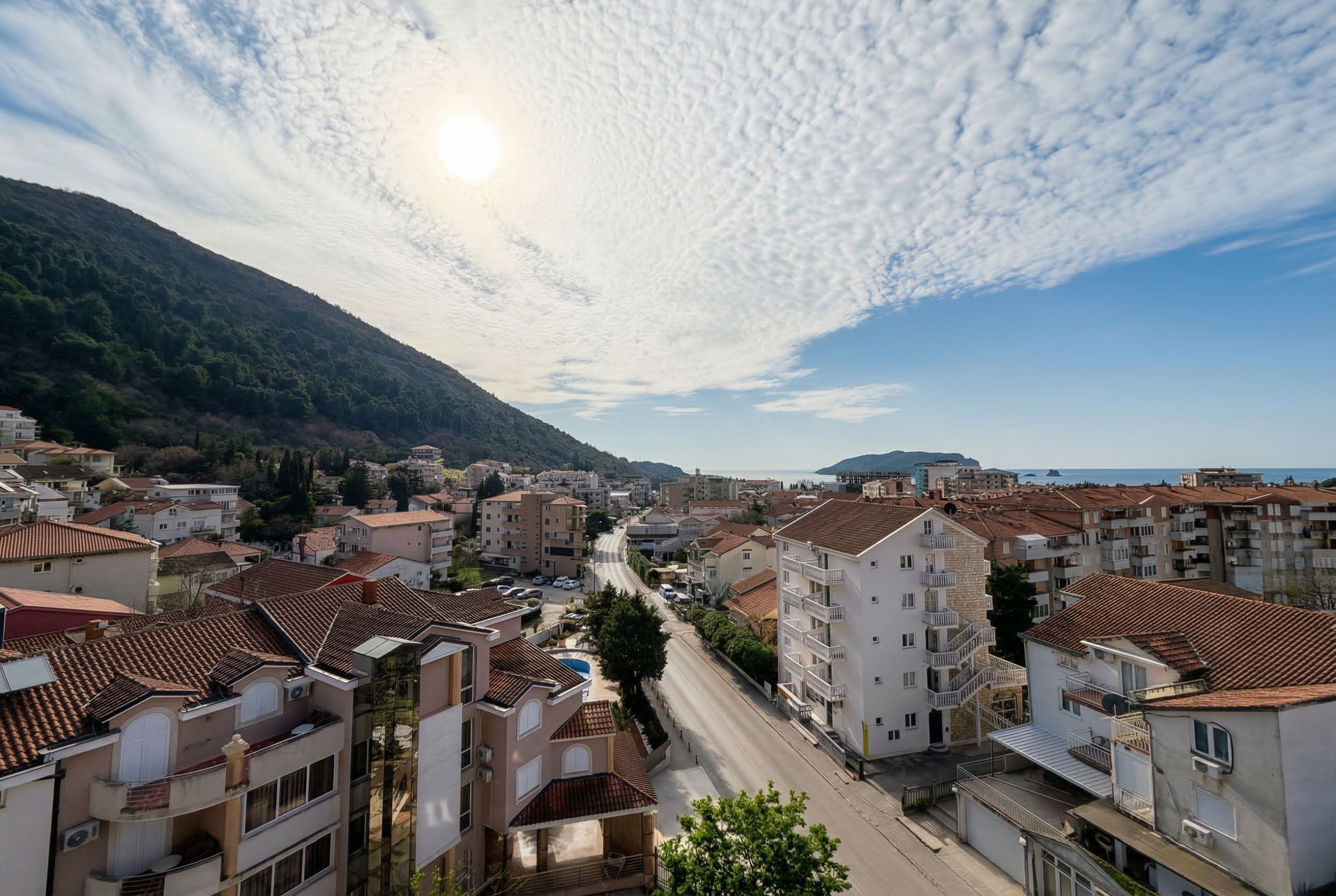 Panoramablick auf die Stadt Budva, Montenegro: Wohngebäude mit Ziegeldächern, Berge und Meereshorizont von der Terrasse aus.
