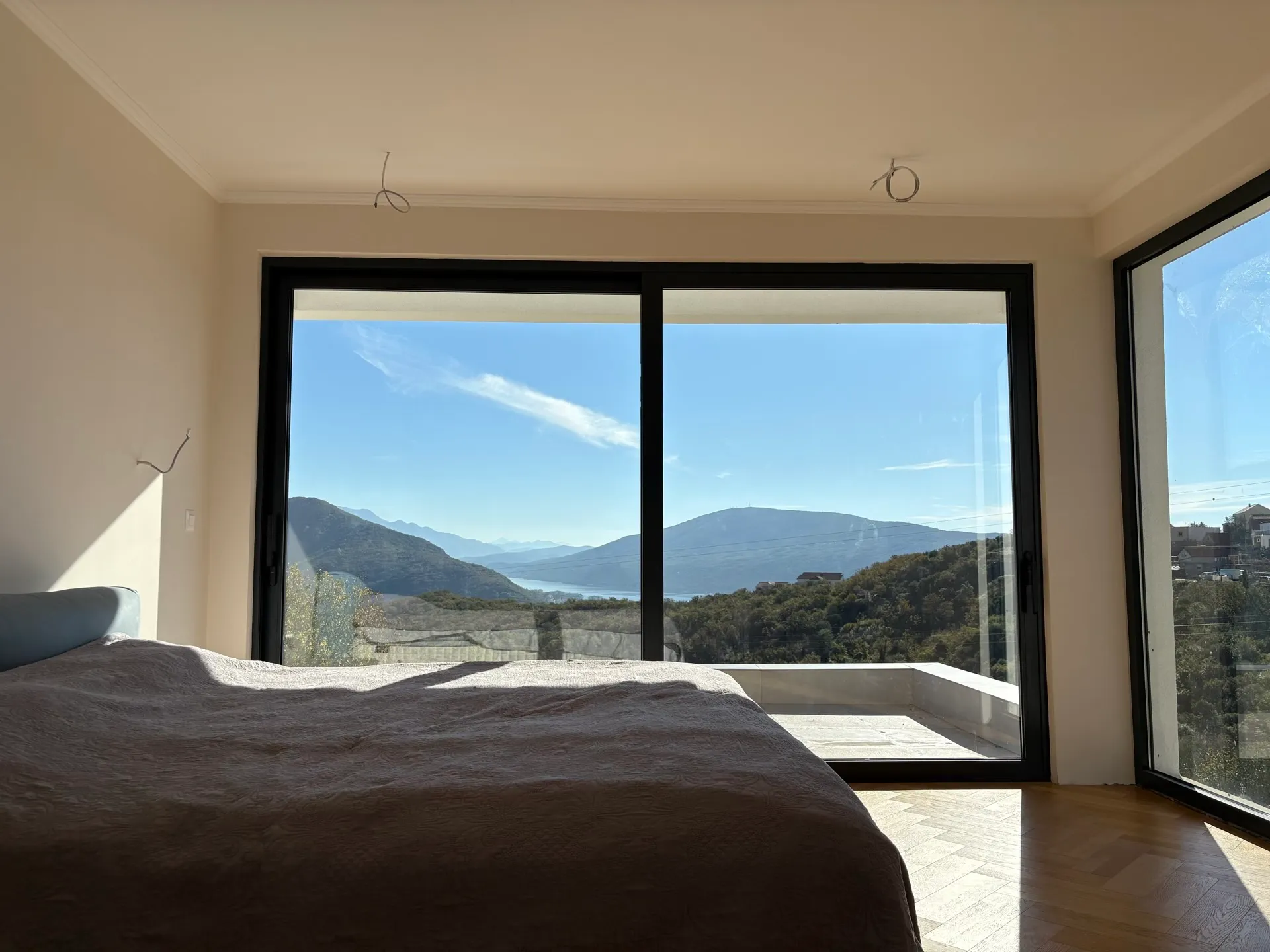 Bedroom in a villa in Herceg Novi, Montenegro: panoramic windows with mountain and sea views, parquet flooring, and a modern interior.