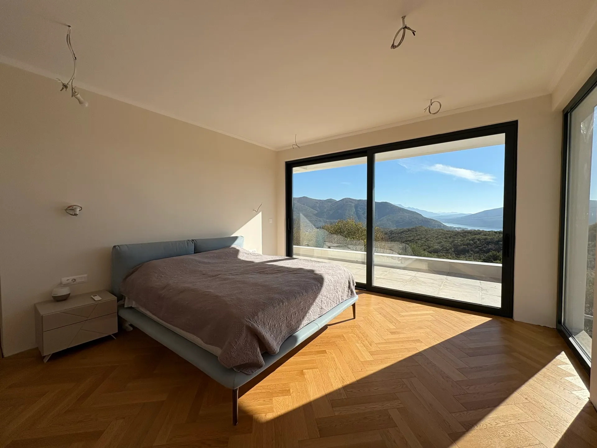 Bedroom in a villa in Herceg Novi, Montenegro: panoramic windows with mountain views, herringbone parquet, and a modern bed.