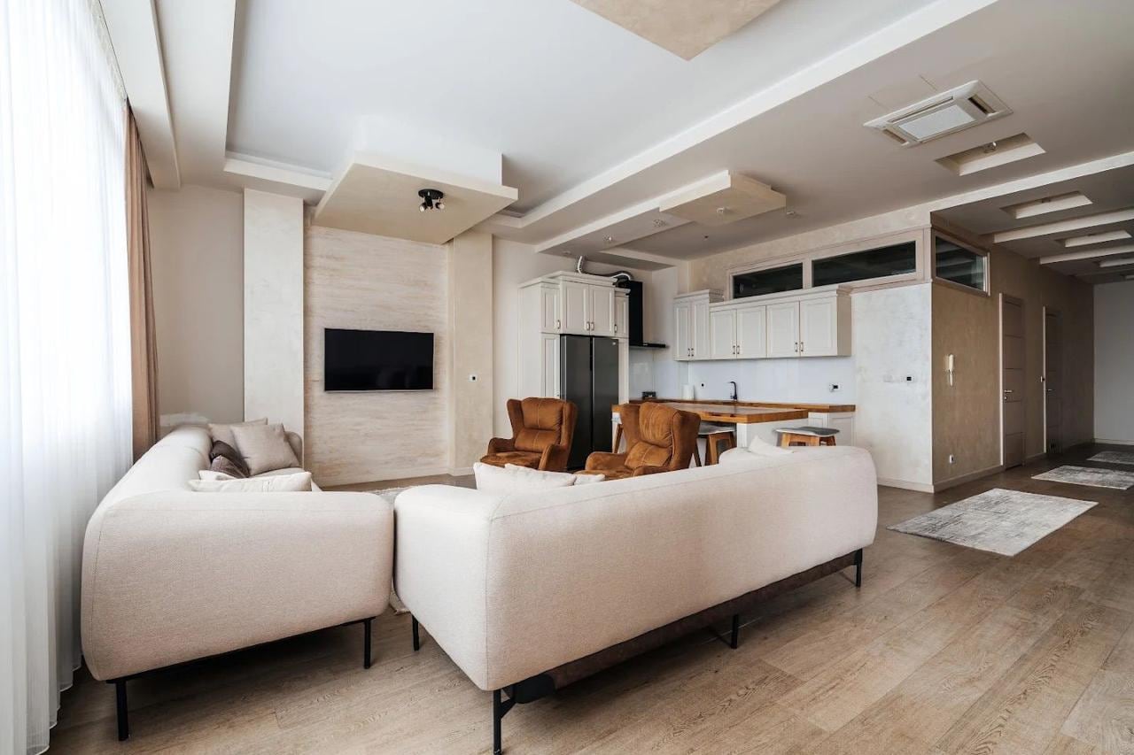 Savremena dnevna soba sa kuhinjom u stanu u Budvi, Crna Gora: svetla sofa, braon fotelje i stilizovan enterijer.