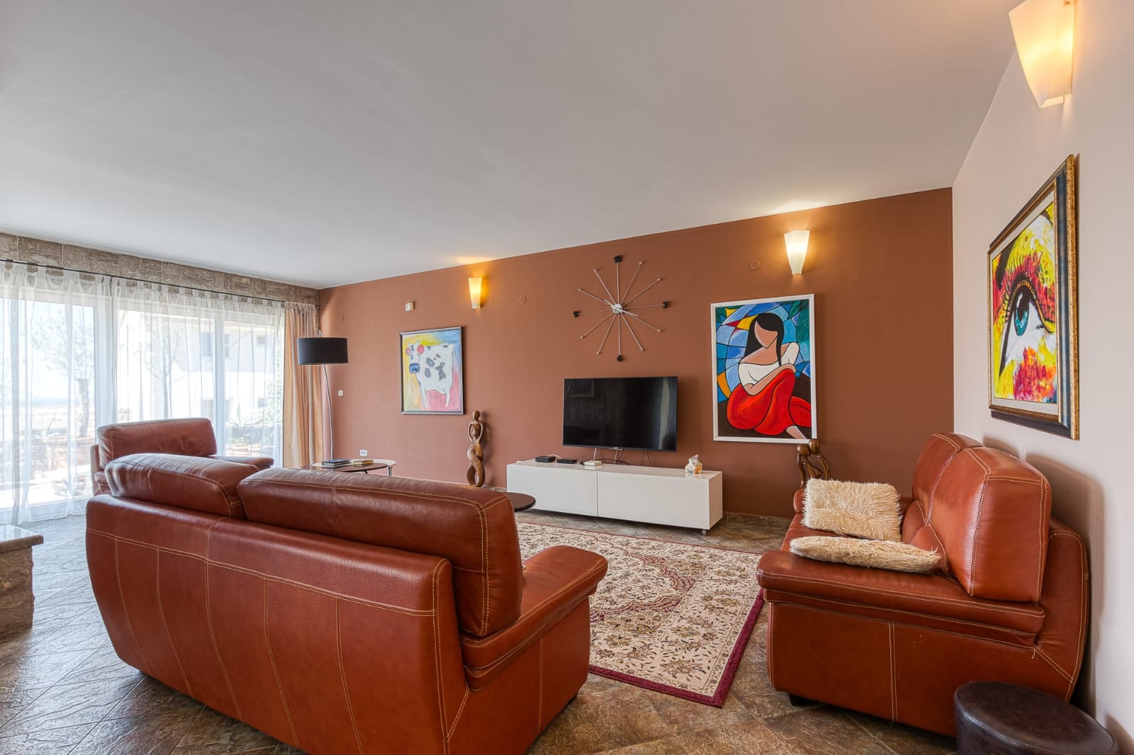 Salon avec canapés en cuir dans une villa à Bečići, Monténégro : intérieur élégant, baies vitrées et décoration murale.