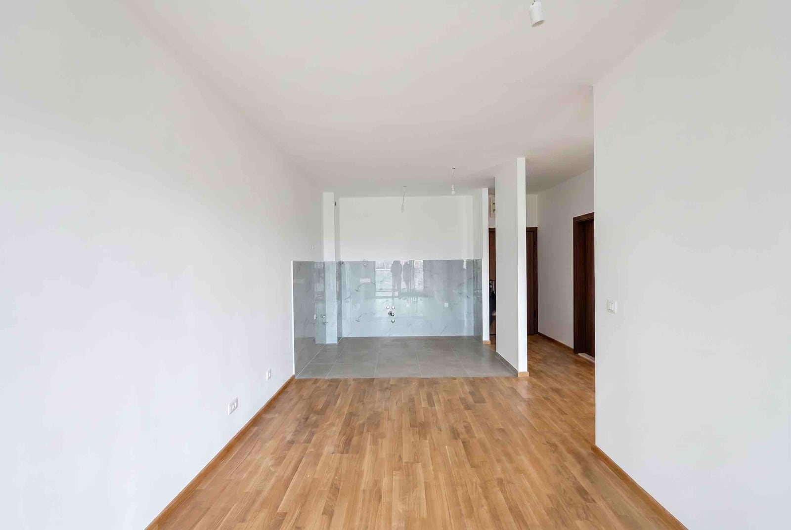 Bright living room with a kitchen area in a new apartment in Budva, Montenegro: parquet flooring and marble-look tile finish.